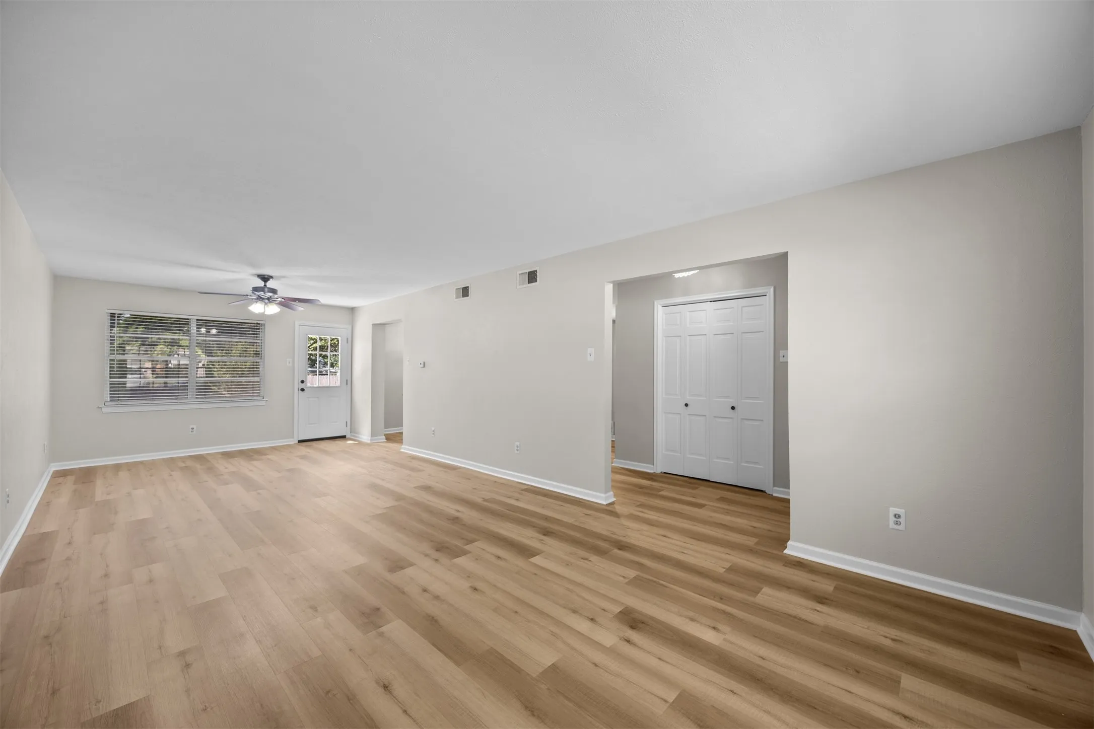 Spacious interior featuring wood-finish flooring, a ceiling fan with integrated lighting, and neutral wall paint
