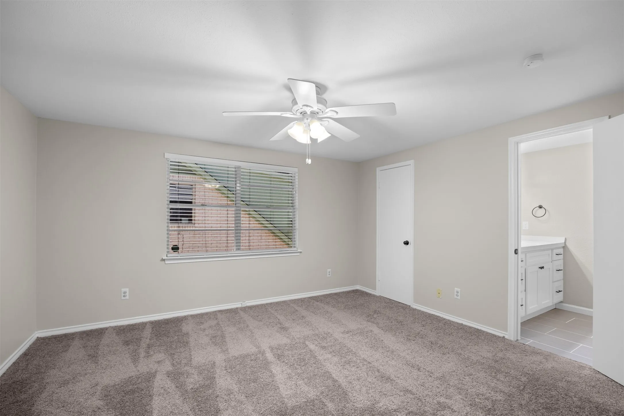 Spacious room featuring neutral carpeting, a ceiling fan with light, and a window with horizontal blinds