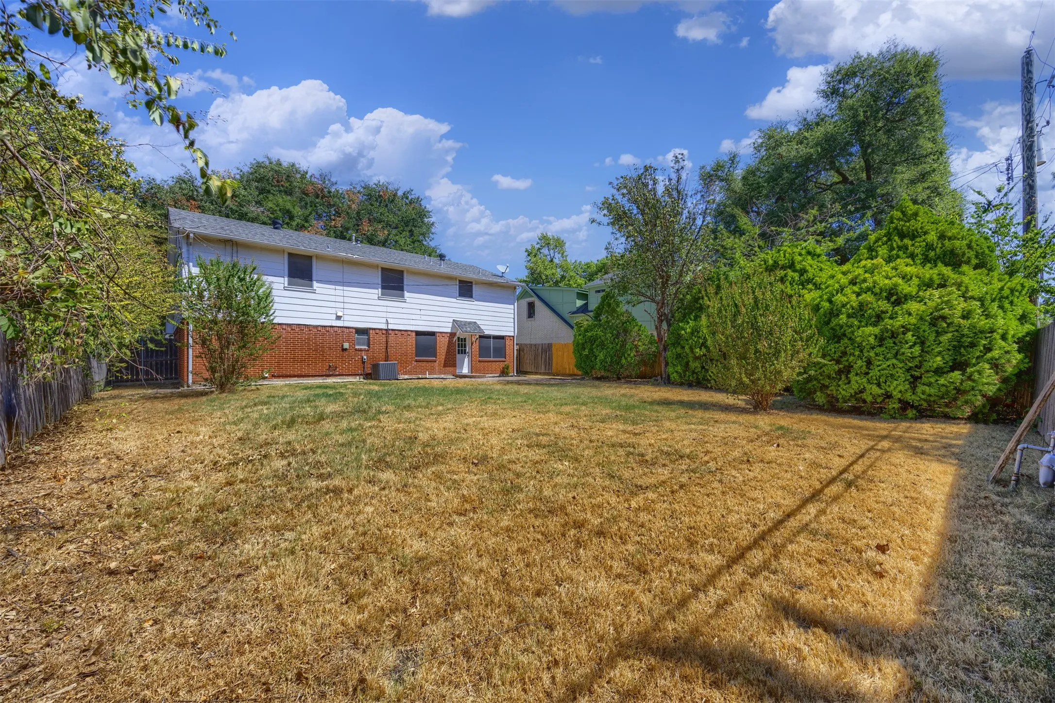 Backyard with mature landscaping, fenced perimeter, and a two-story structure featuring brick and siding