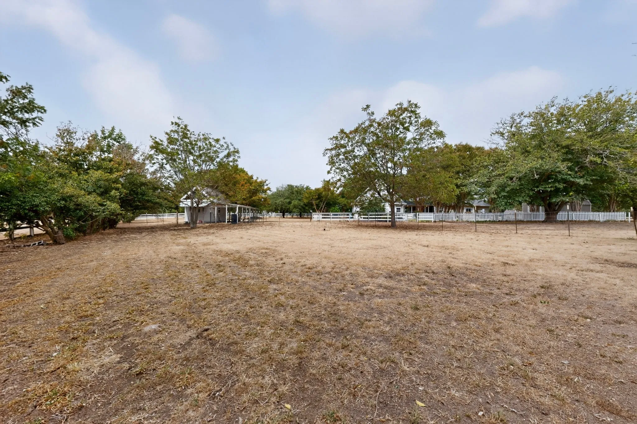 Expansive outdoor area with a white picket fence, mature trees, and a visible outbuilding