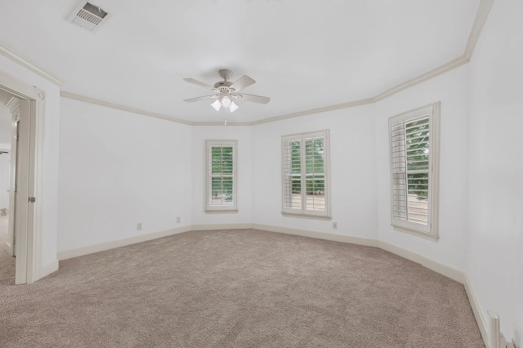 Neutral-toned carpeted flooring, multiple windows with plantation shutters, crown molding, and a ceiling fan with integrated lighting