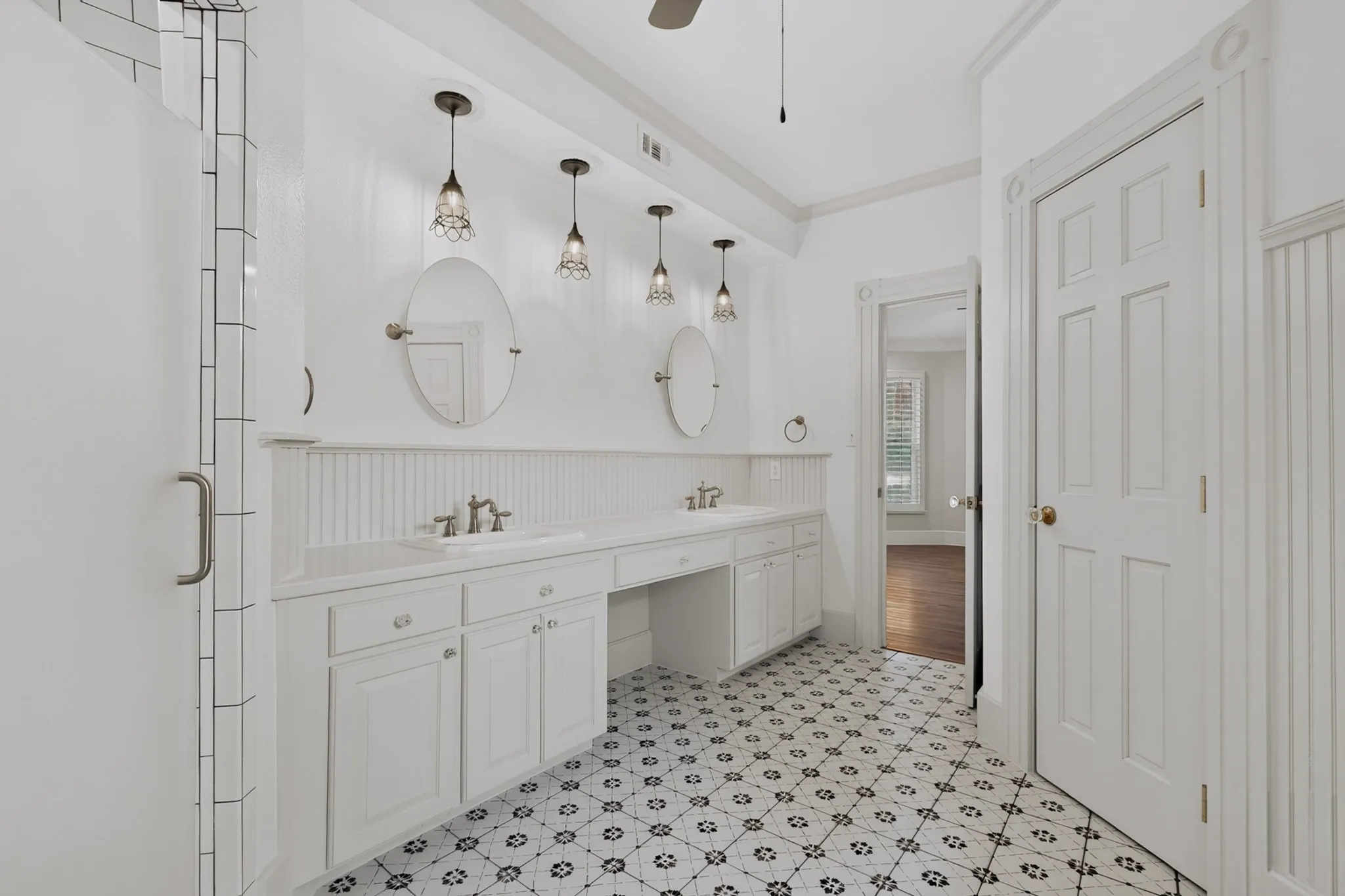 Spacious bathroom featuring a dual vanity with white cabinetry, patterned floor tiling, and a shower enclosure with subway tile