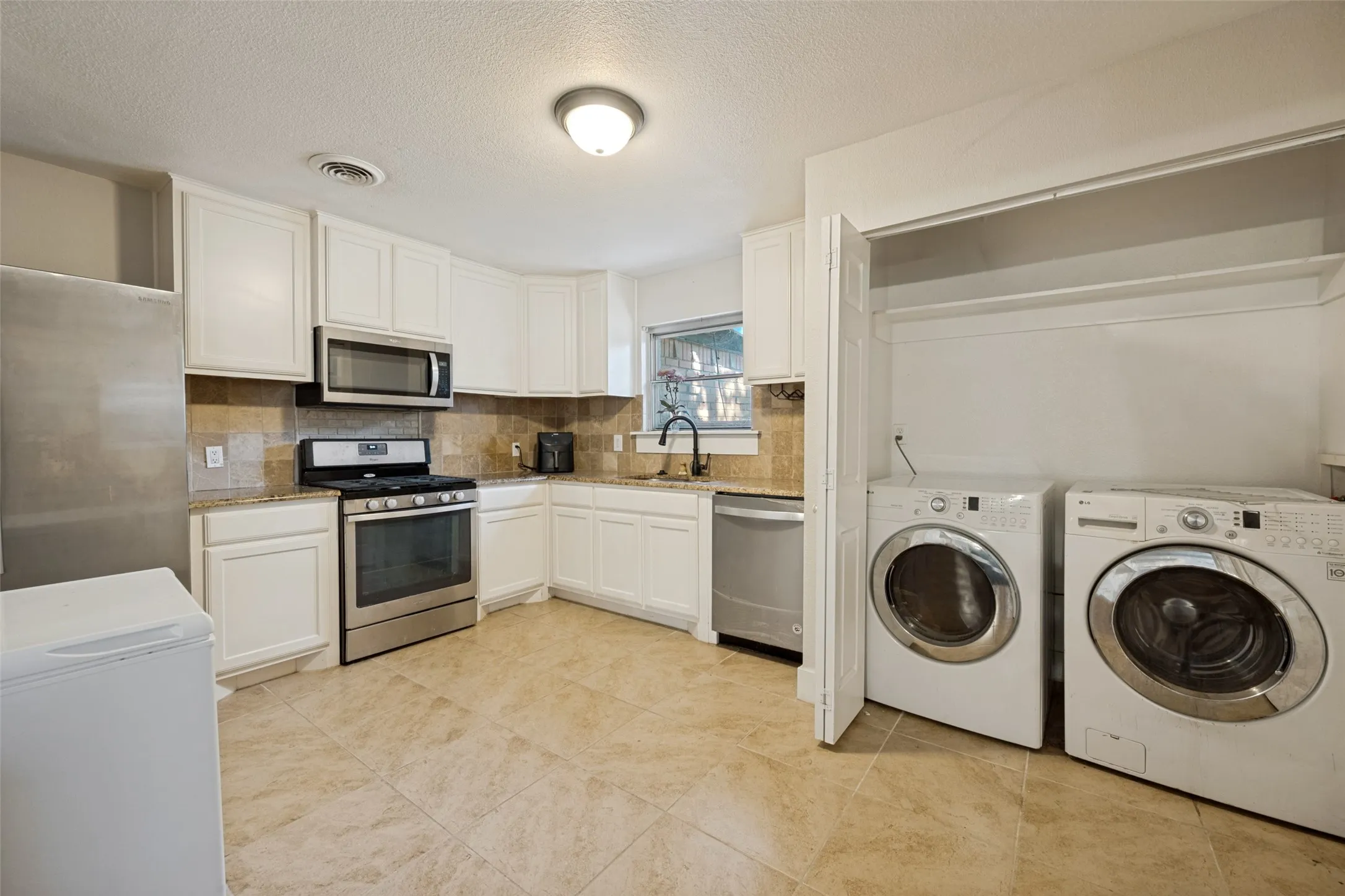 Kitchen with white cabinetry, stainless steel appliances, tile flooring, and a tile backsplash
