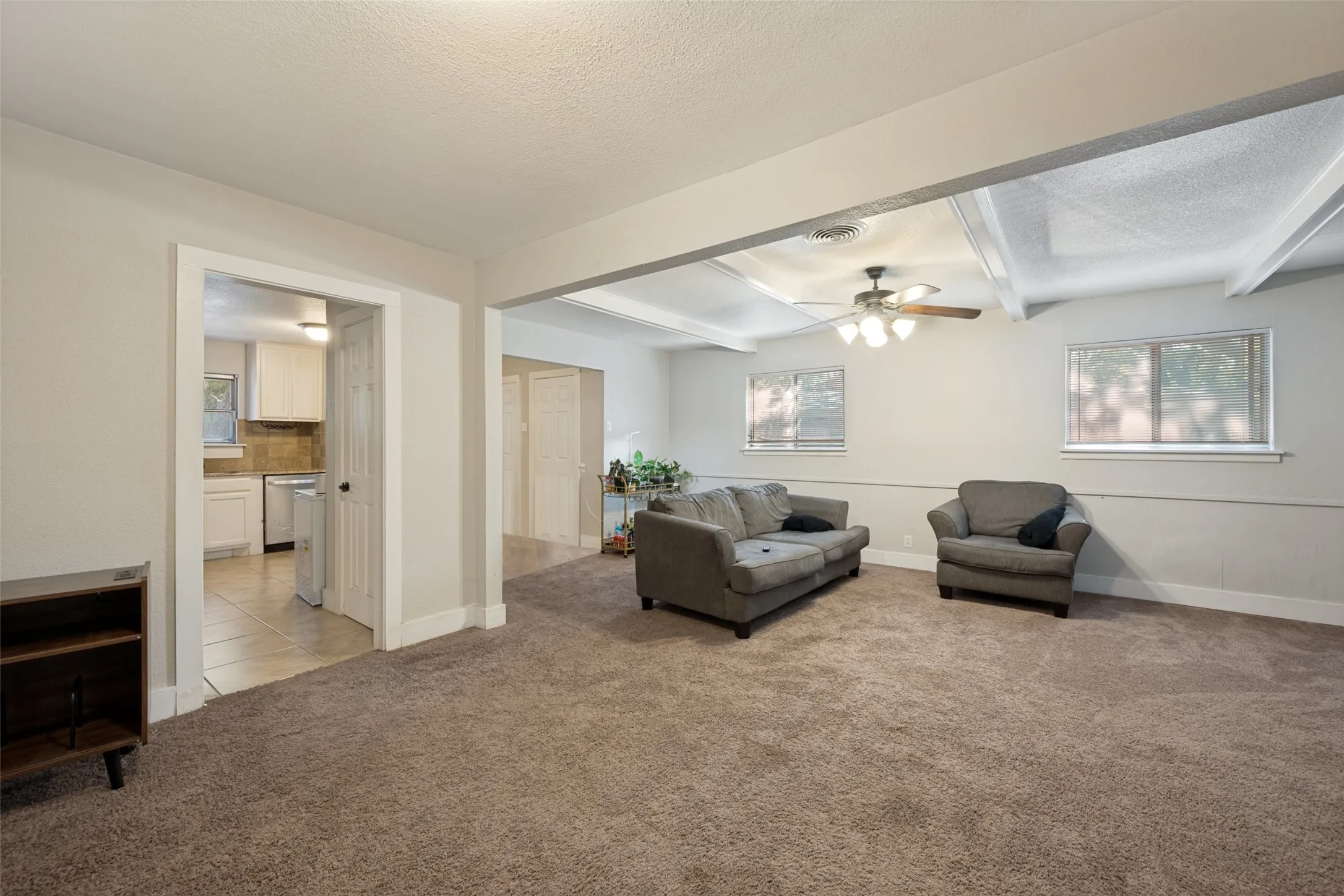 Open-concept living space with carpeted flooring, a ceiling fan, and exposed beams