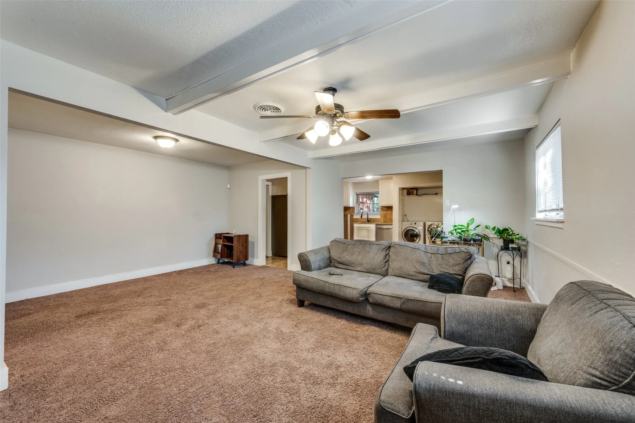Expansive room featuring exposed ceiling beams, a ceiling fan with integrated lighting, and neutral wall tones