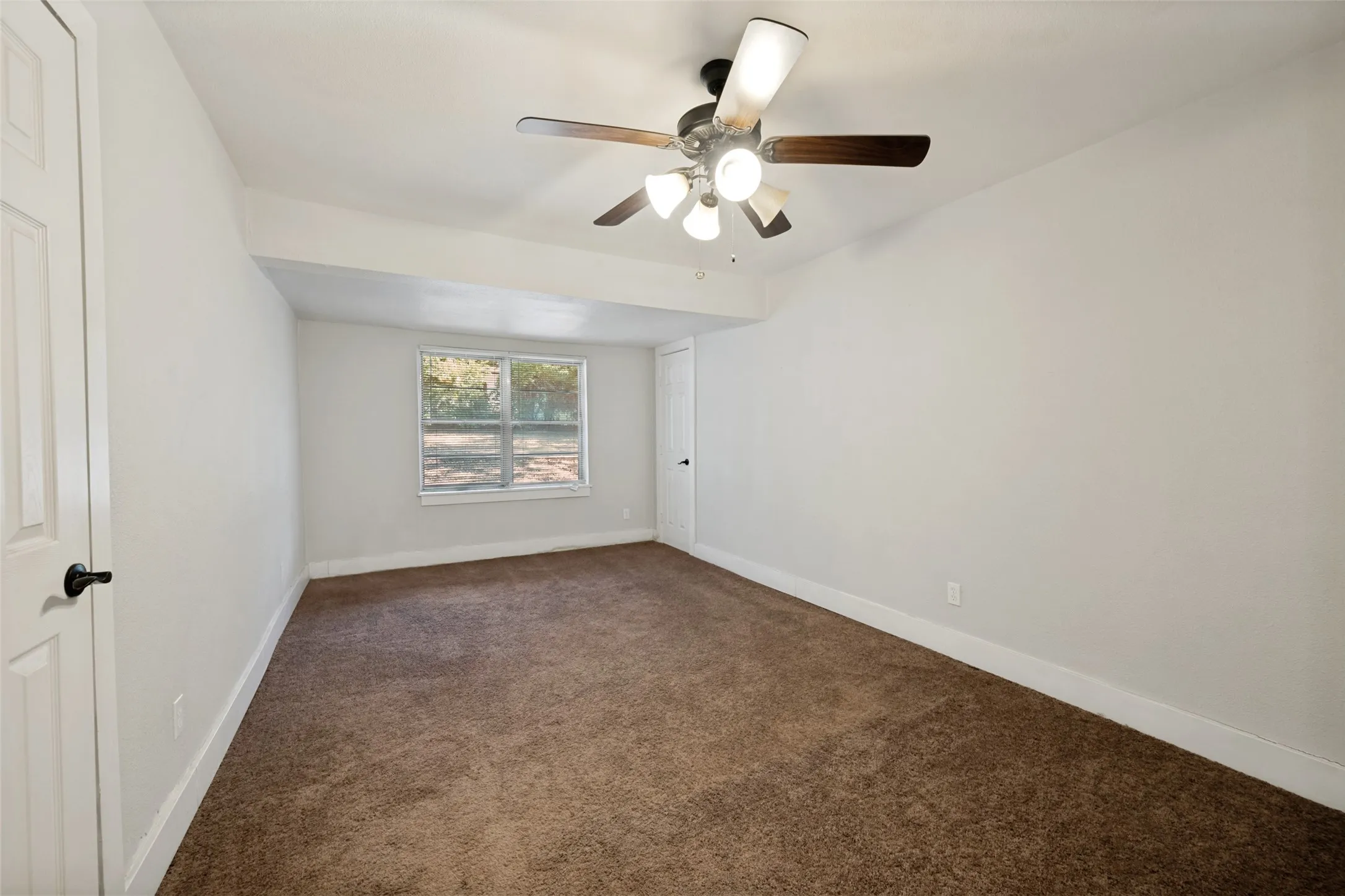 Recessed window with exterior scenery, overhead ceiling fan with light fixture, white interior doors, and carpet flooring