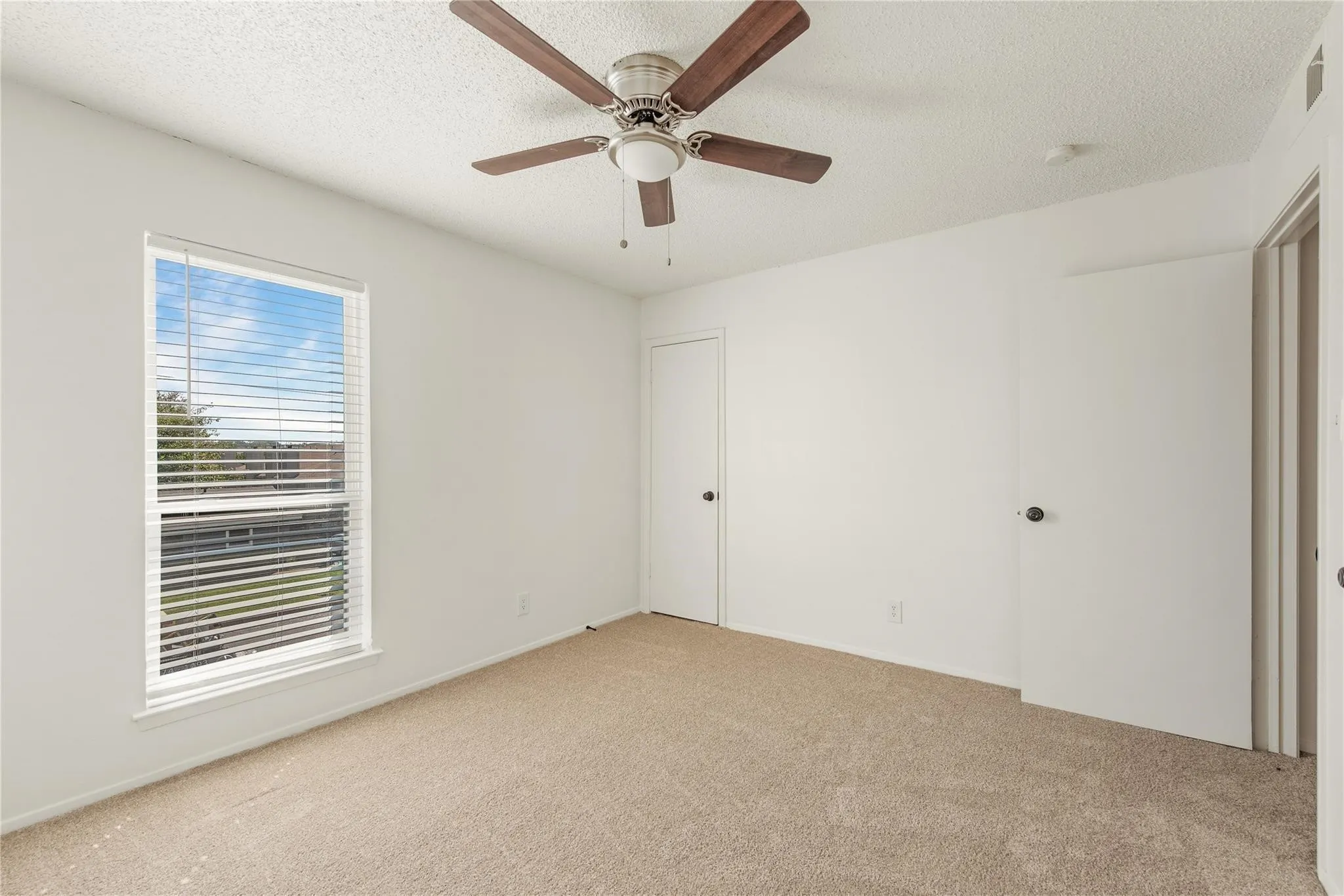 Carpeted flooring, white walls, single window with blinds, ceiling fan, and multiple white doors