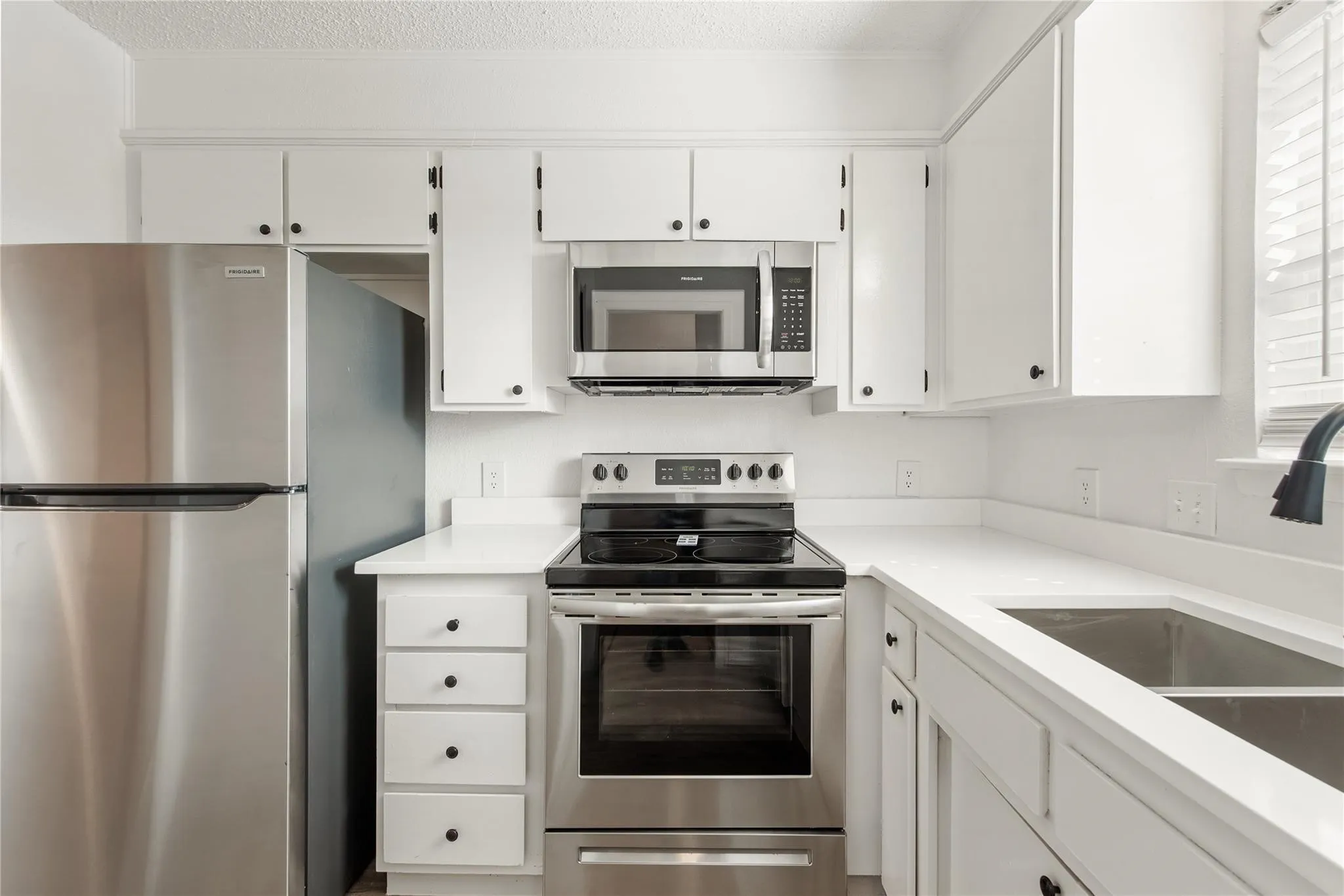 White cabinetry, stainless steel appliances, solid surface countertops, double basin sink, and a built-in microwave