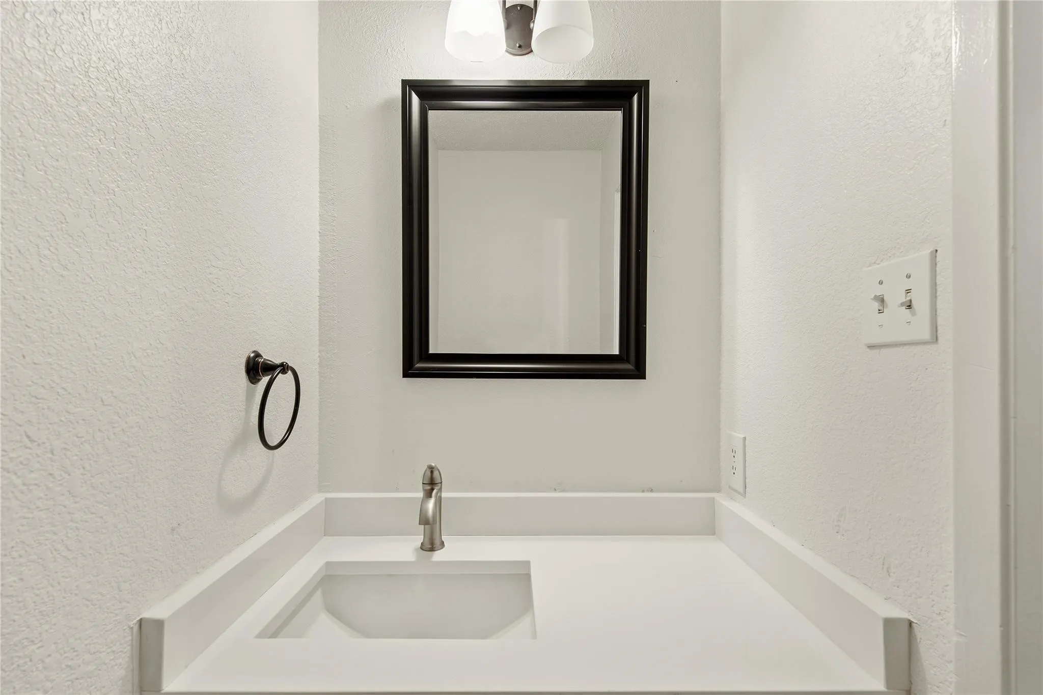 White countertop with an integrated rectangular sink, brushed nickel faucet, framed mirror, and wall-mounted light fixture
