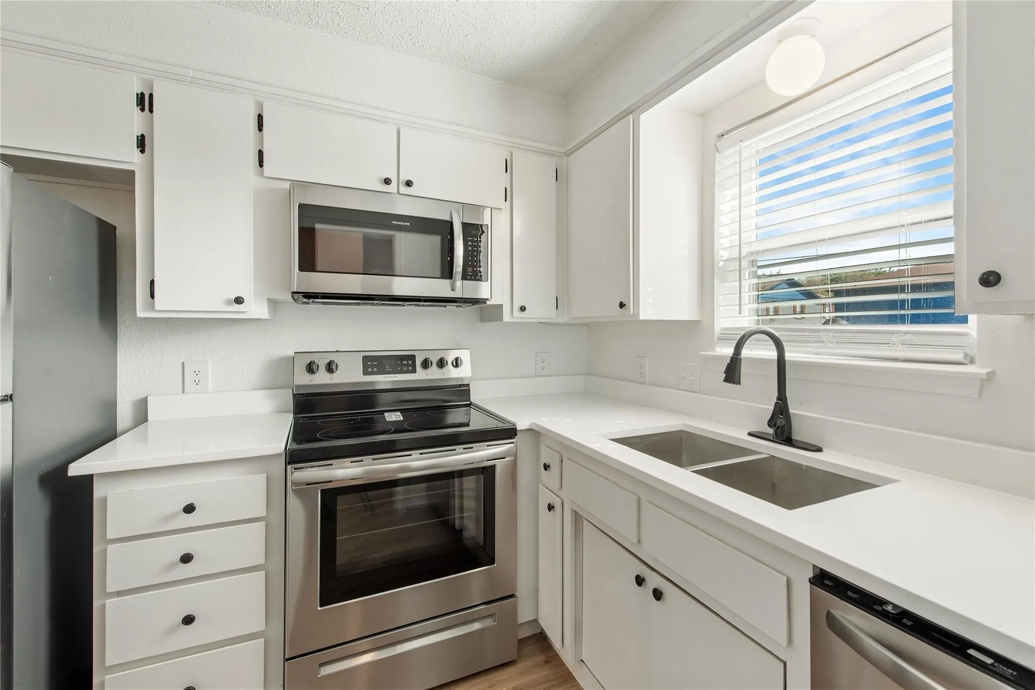 White cabinetry, stainless steel appliances, dual basin sink, white countertops, and black hardware