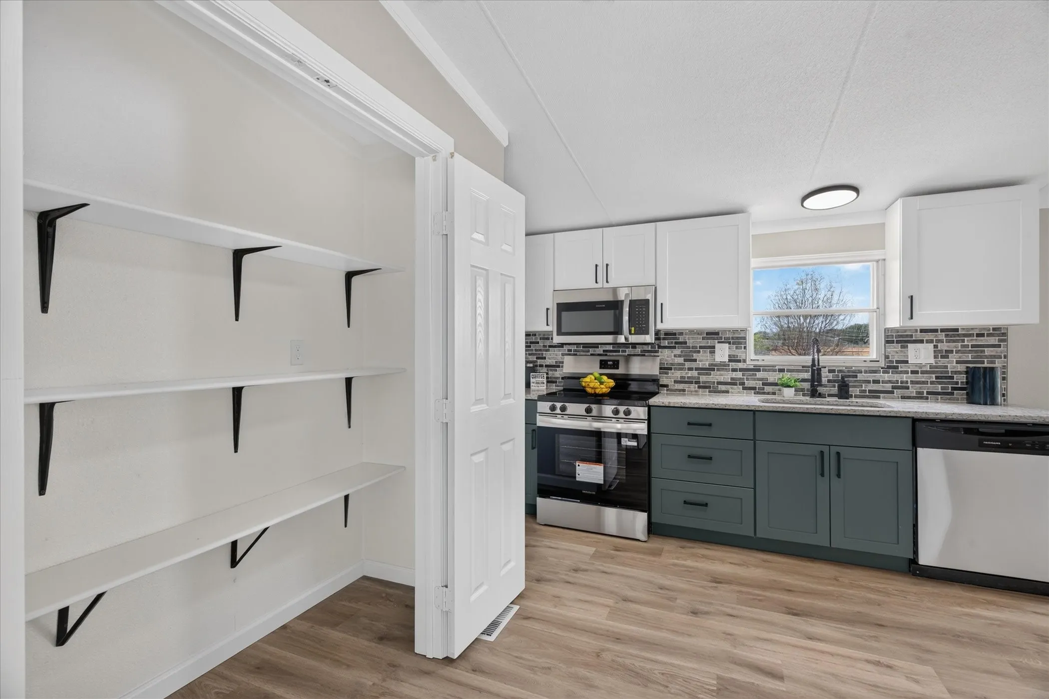 Kitchen featuring wood-finish flooring, two-tone cabinetry, stainless steel appliances, a tile backsplash, and a built-in pantry with shelving