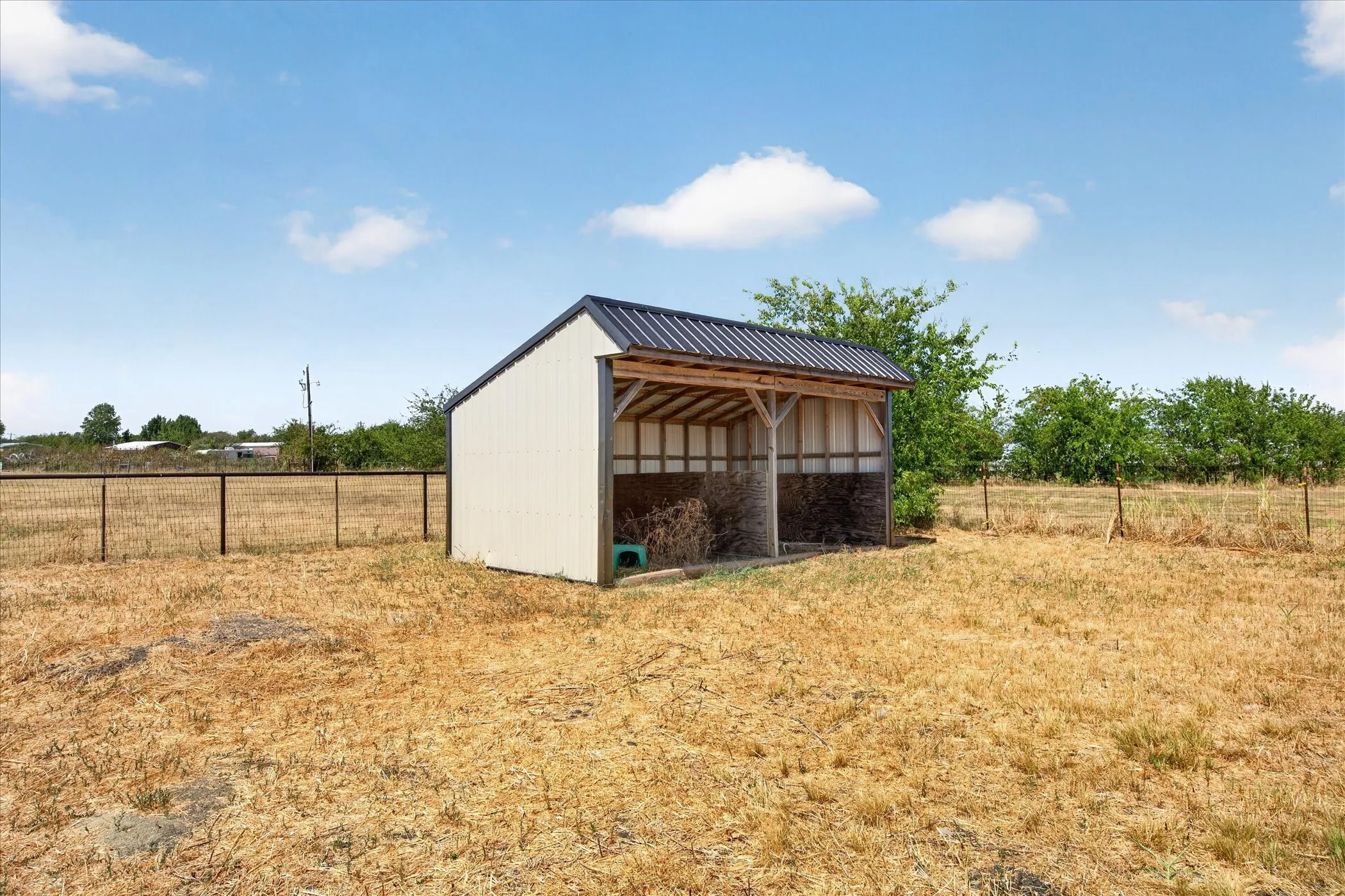 Freestanding shelter with a metal roof and open-sided design, situated within a fenced perimeter