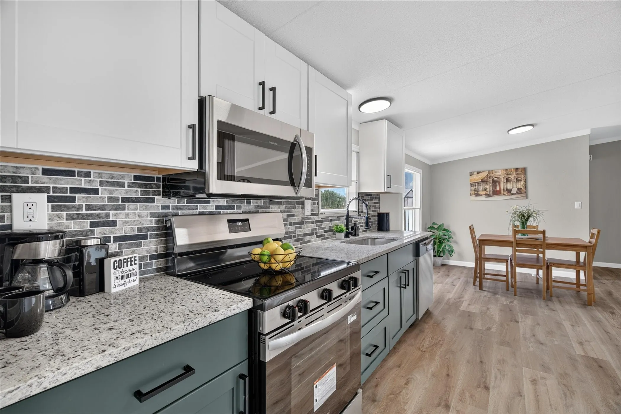 Kitchen with two-tone cabinetry, stainless steel appliances, granite-style countertops, and a tile backsplash