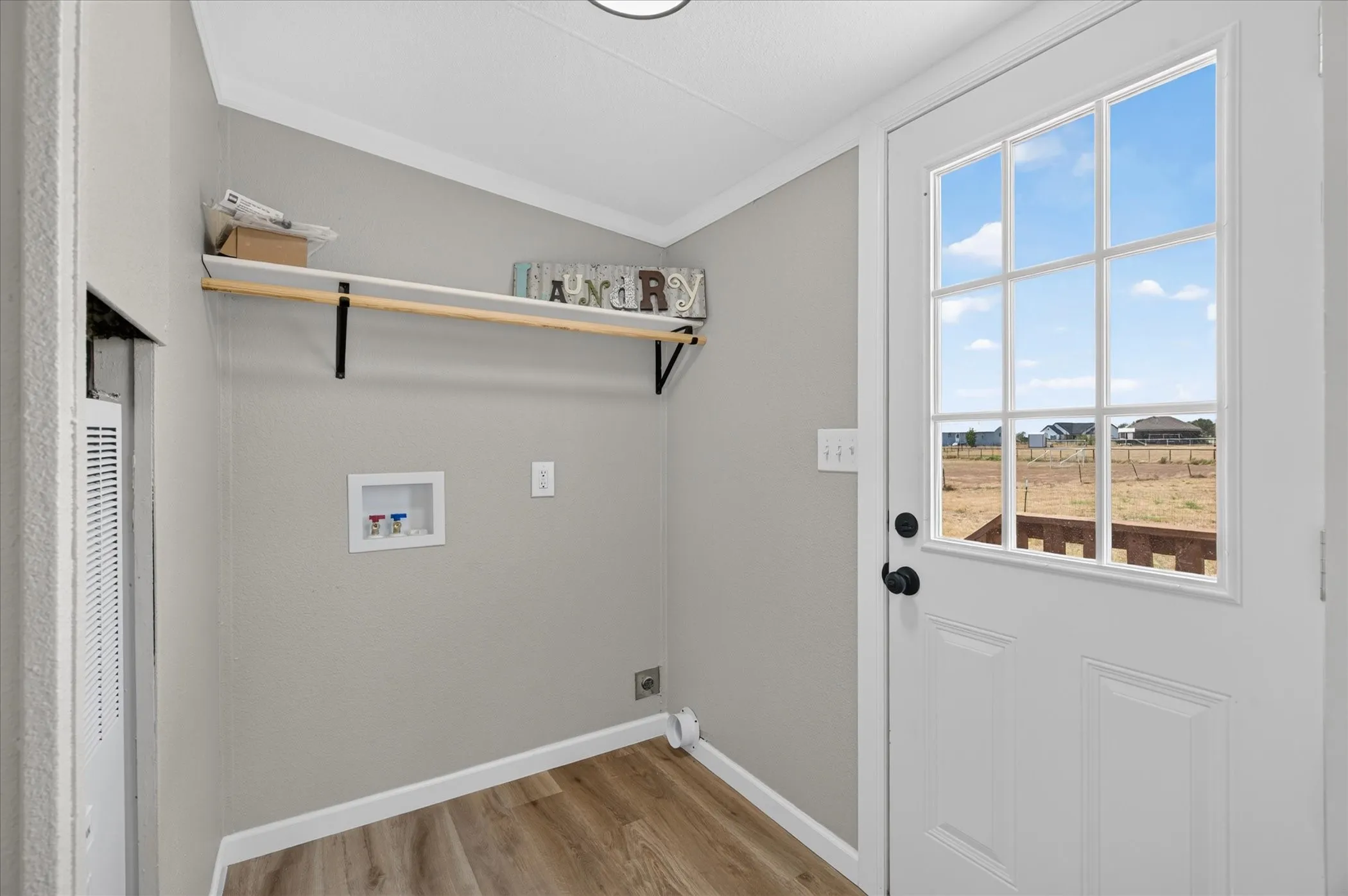 Laundry area featuring wood-finish flooring, a built-in shelf with a hanging rod, and a white paneled door with glass inserts