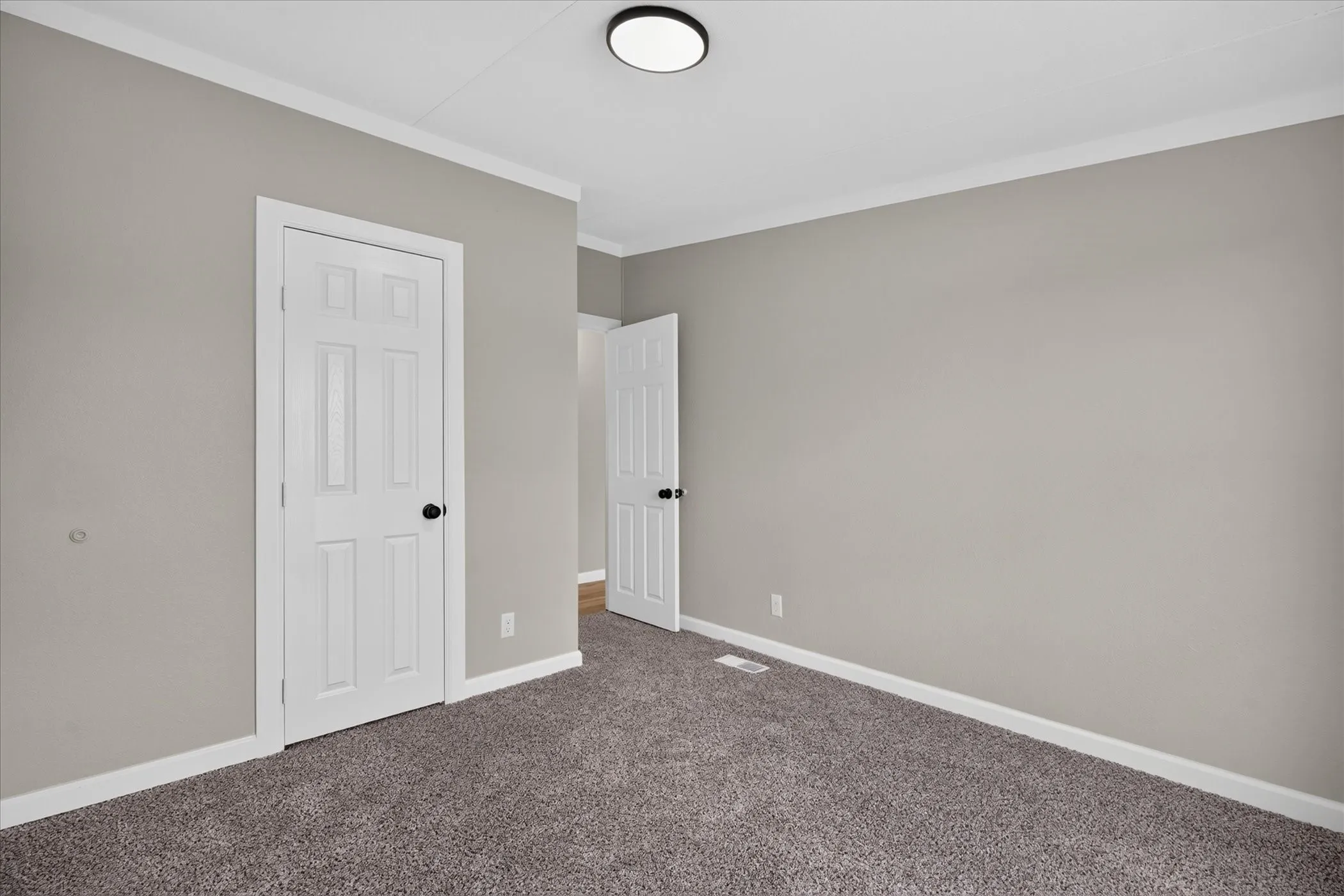 Recessed lighting, plush carpet flooring, light gray wall paint, crisp white trim, and a paneled door with matte black hardware