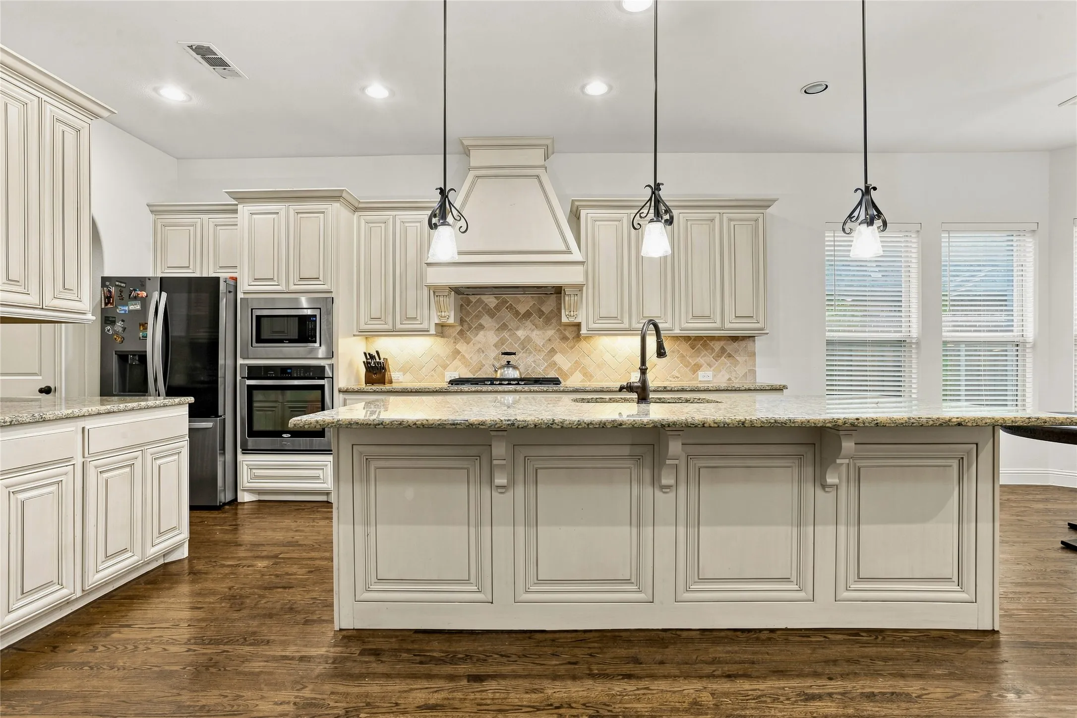 Kitchen featuring light-toned cabinetry, a spacious island with a built-in sink, stainless steel appliances, and wood-finish flooring