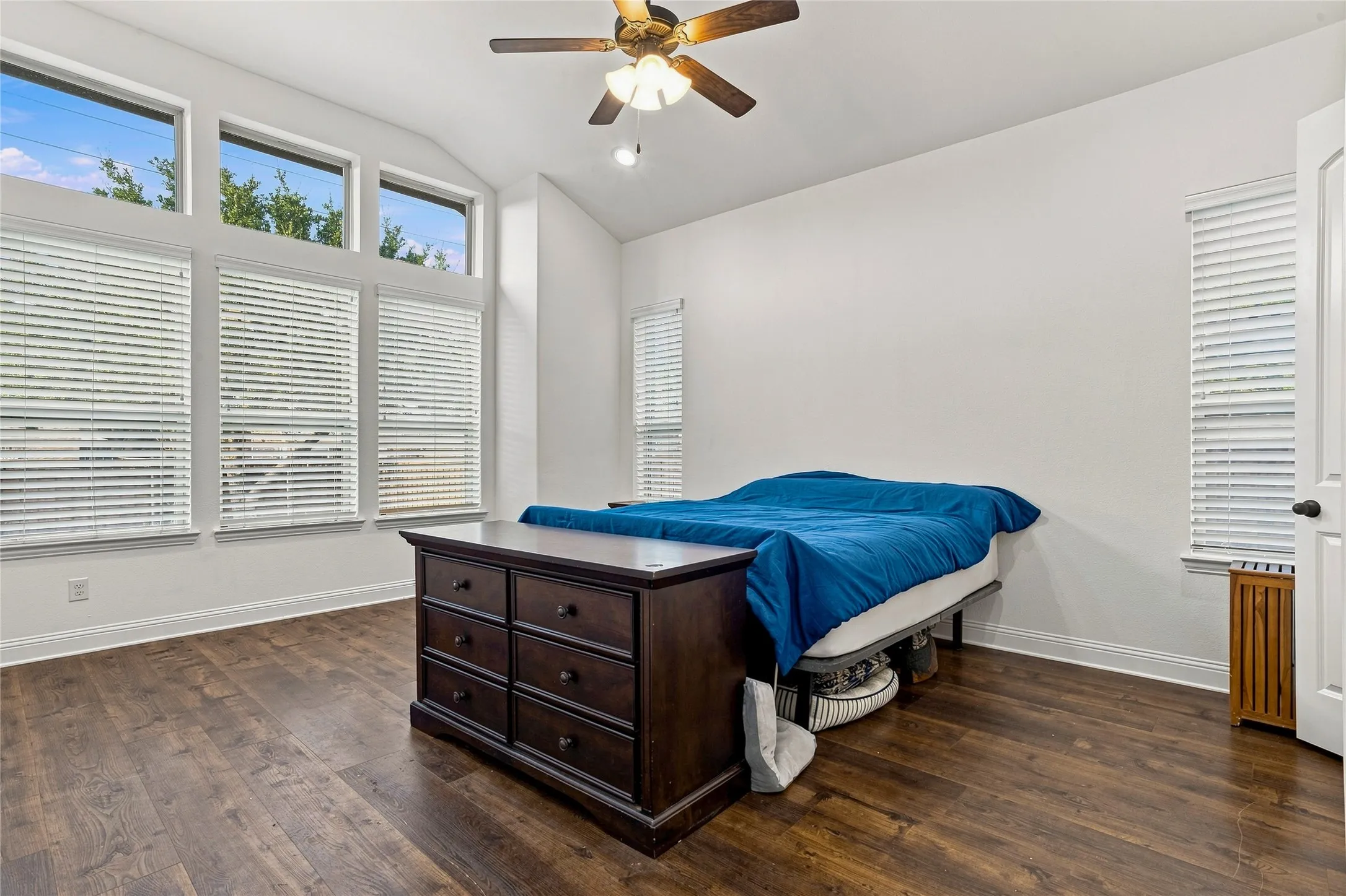 Vaulted ceiling with a ceiling fan, wood-finish flooring, and multiple windows