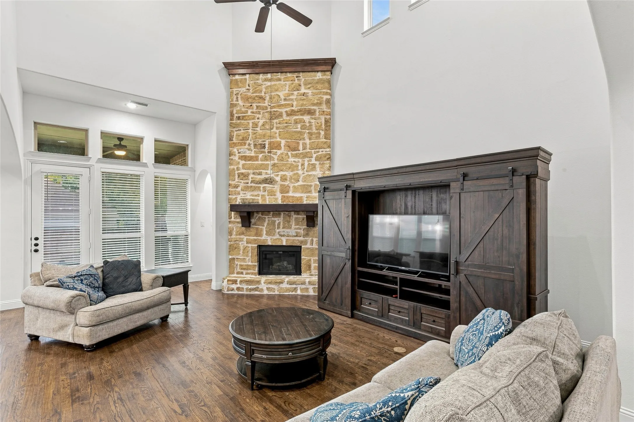 Vaulted ceiling, stone-clad fireplace with wood mantel, wood-finish flooring, built-in entertainment center, and multiple windows