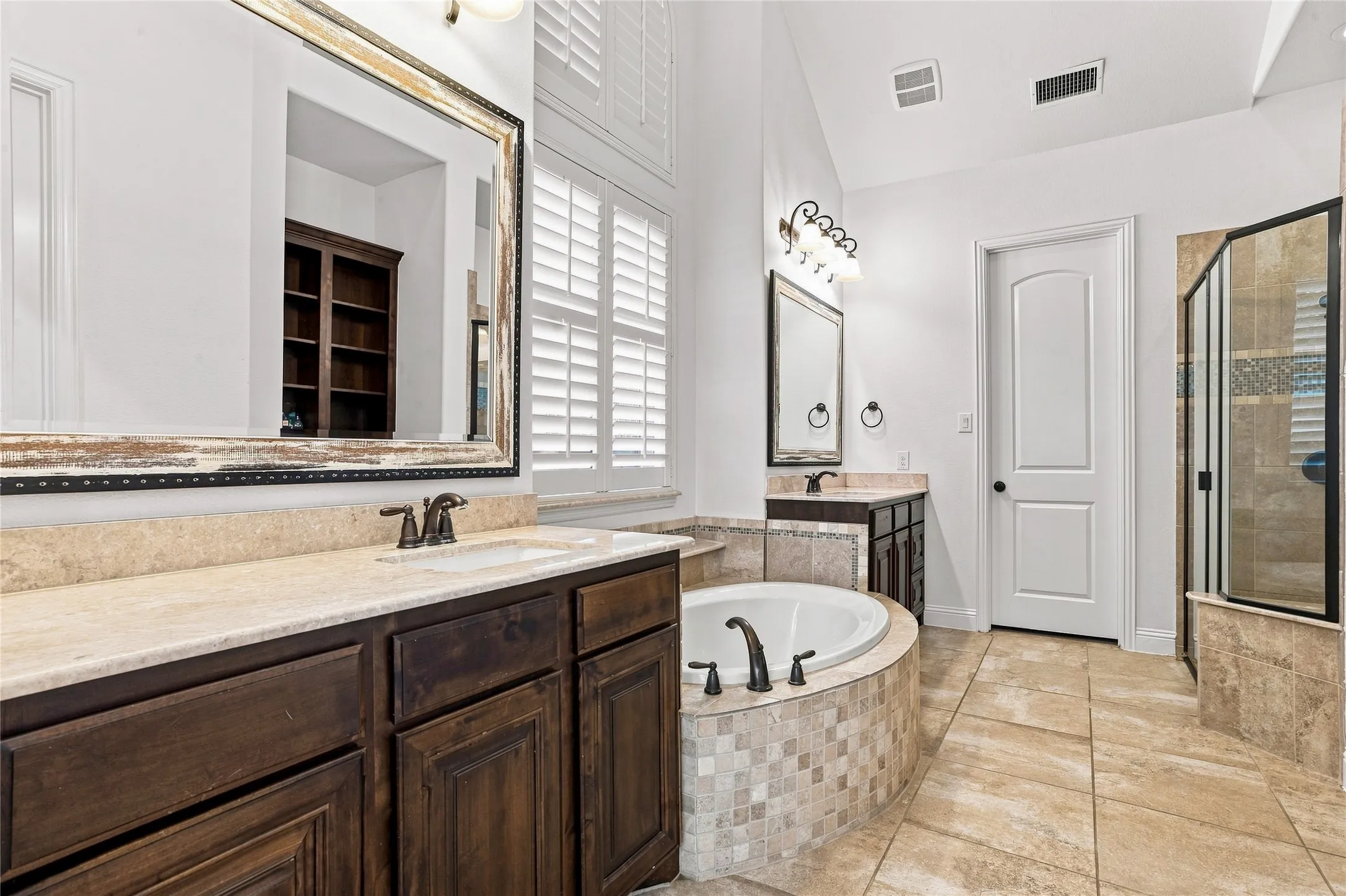 Dual vanity with light-toned countertops, dark wood-finish cabinetry, and framed mirrors