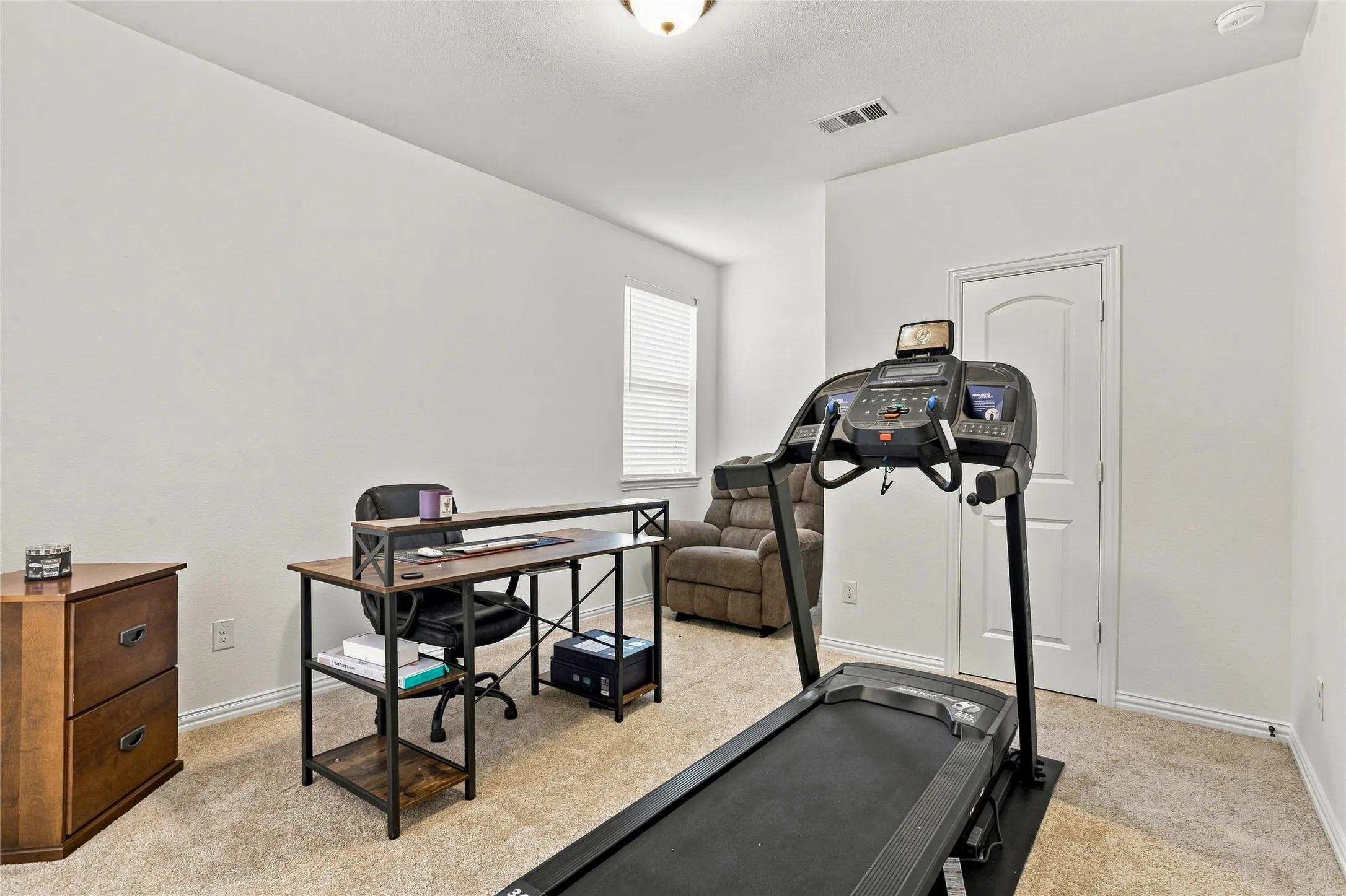 Carpeted flooring with white wall finishes, single window with blinds, and a white interior door