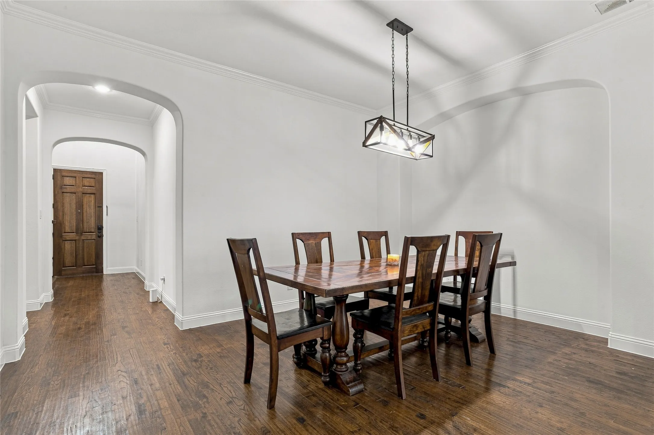 Hardwood flooring, arched doorways, crown molding, modern linear chandelier, and a paneled entry door