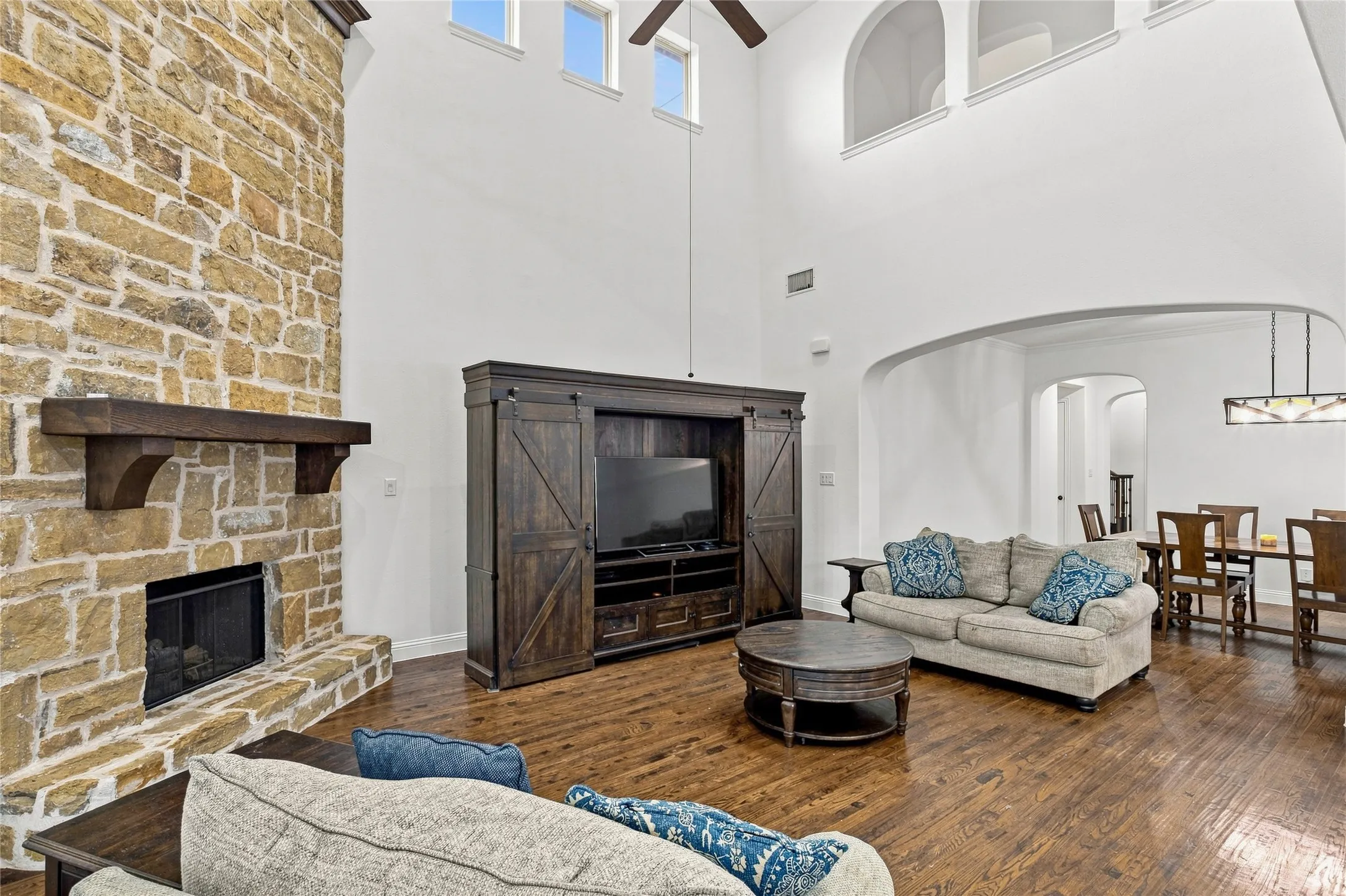 Vaulted ceilings with clerestory windows, stone-clad fireplace with wood mantle, rich wood-finish flooring, and arched doorways