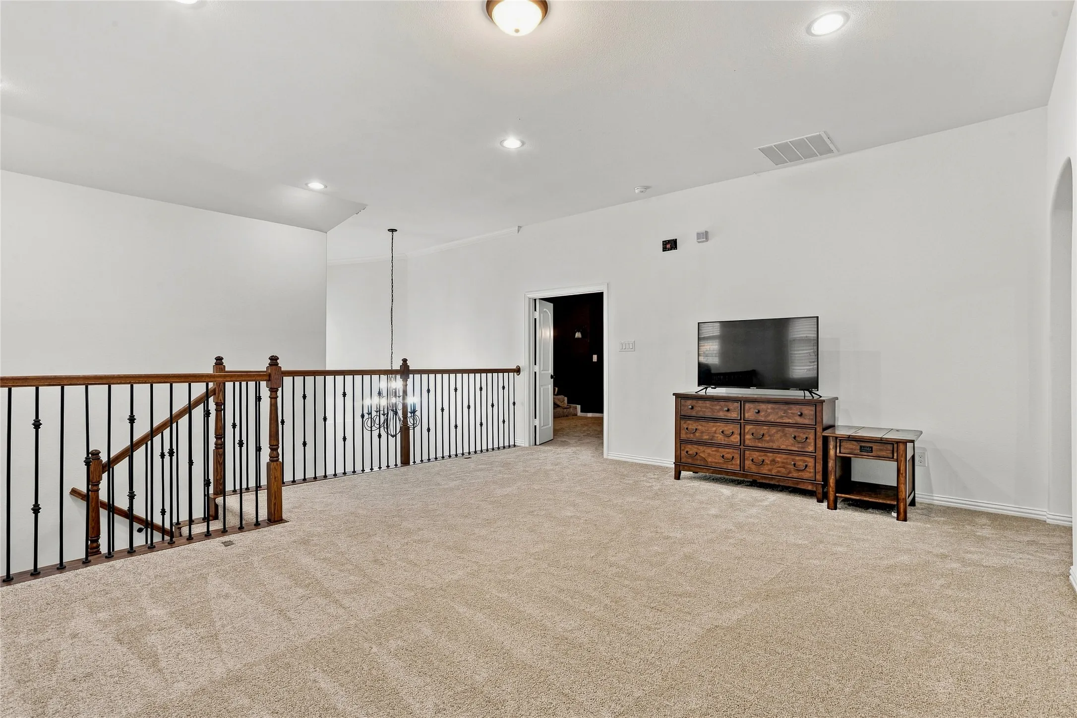 Carpeted open area with recessed lighting, a chandelier, and a wood and wrought iron staircase railing