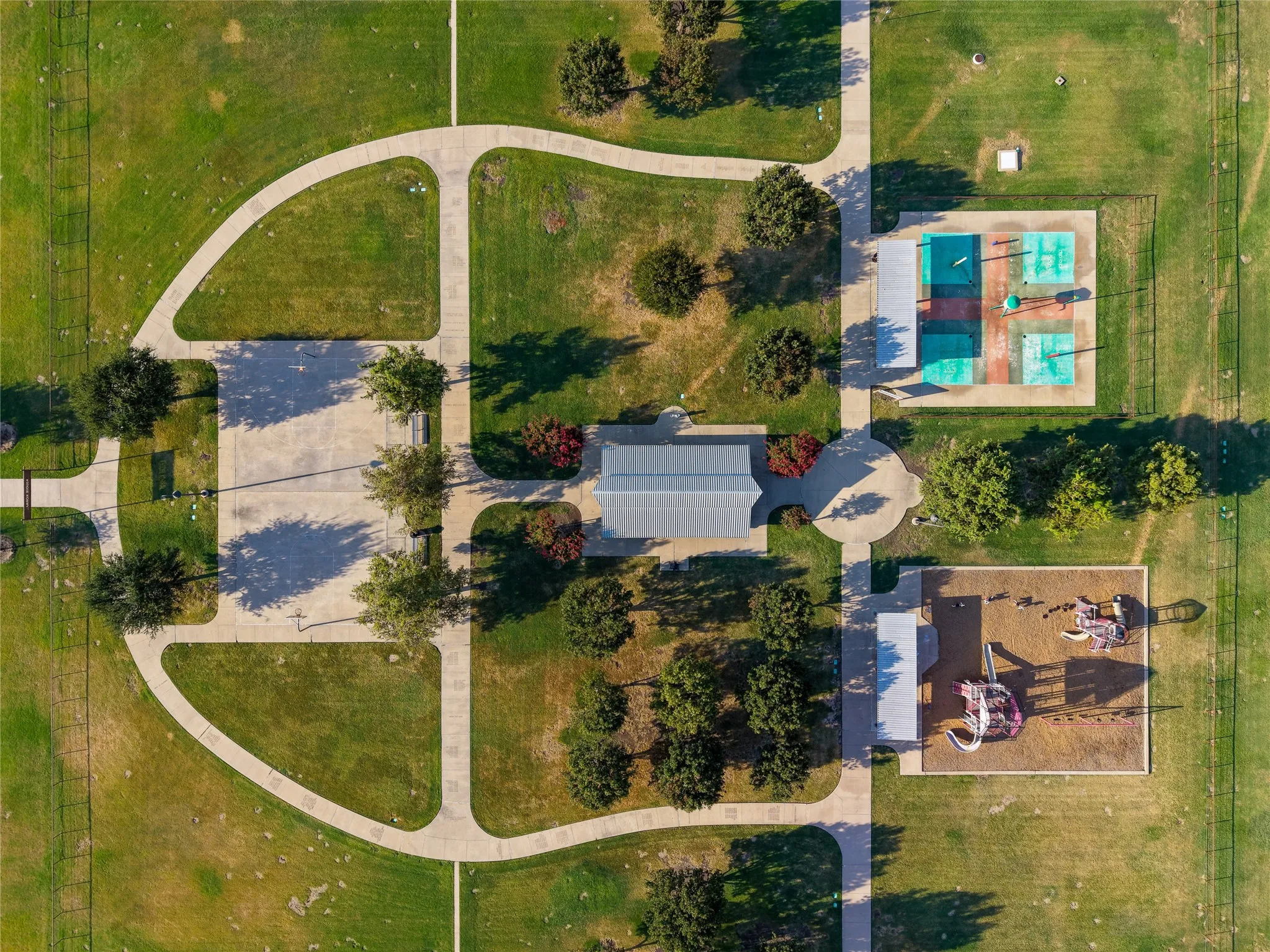 Expansive green spaces with paved walking paths, multiple sports courts, a shaded pavilion, and a dedicated play area