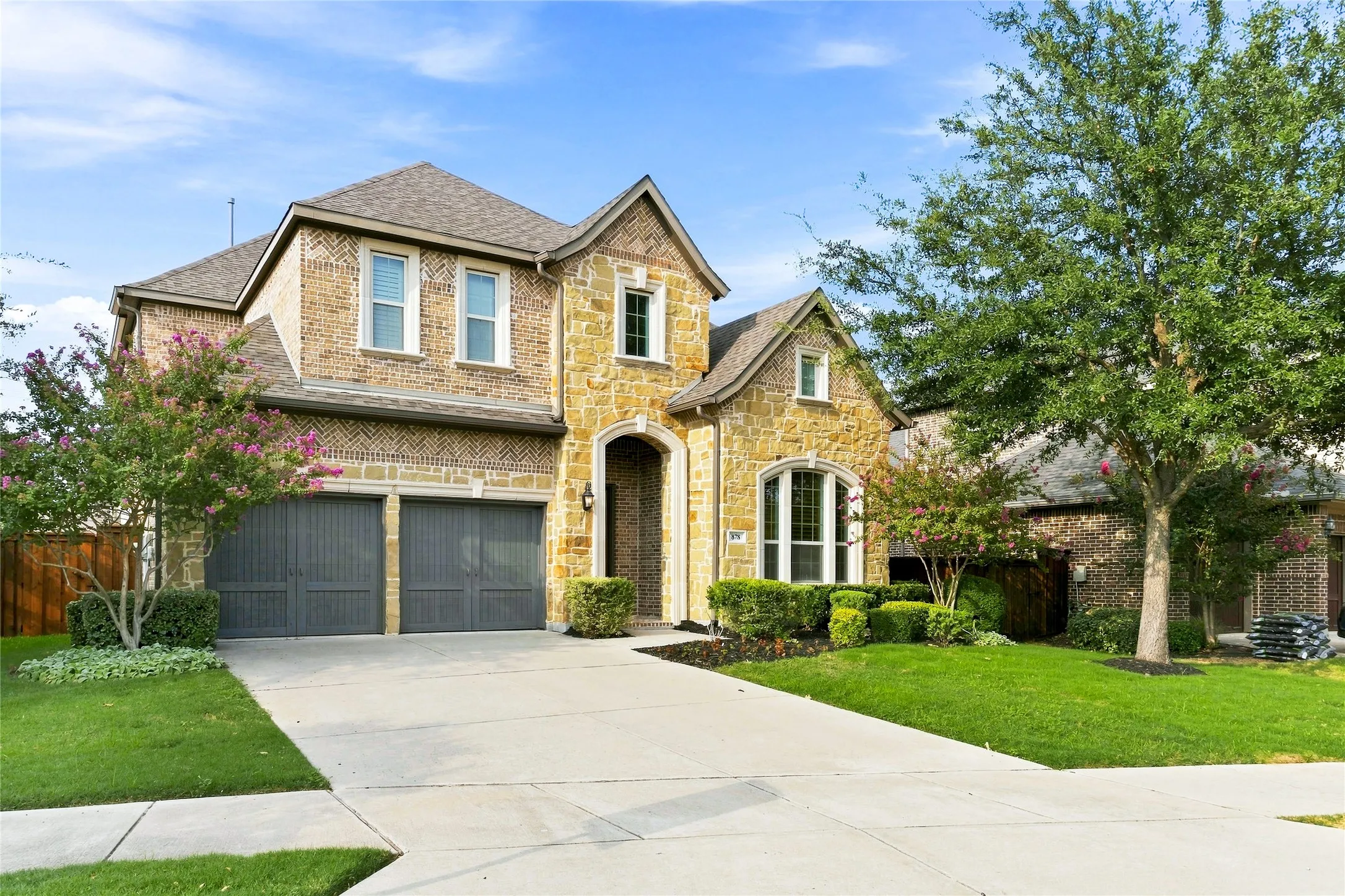 Two-story residence featuring a brick and stone facade, arched entry, and a two-car garage