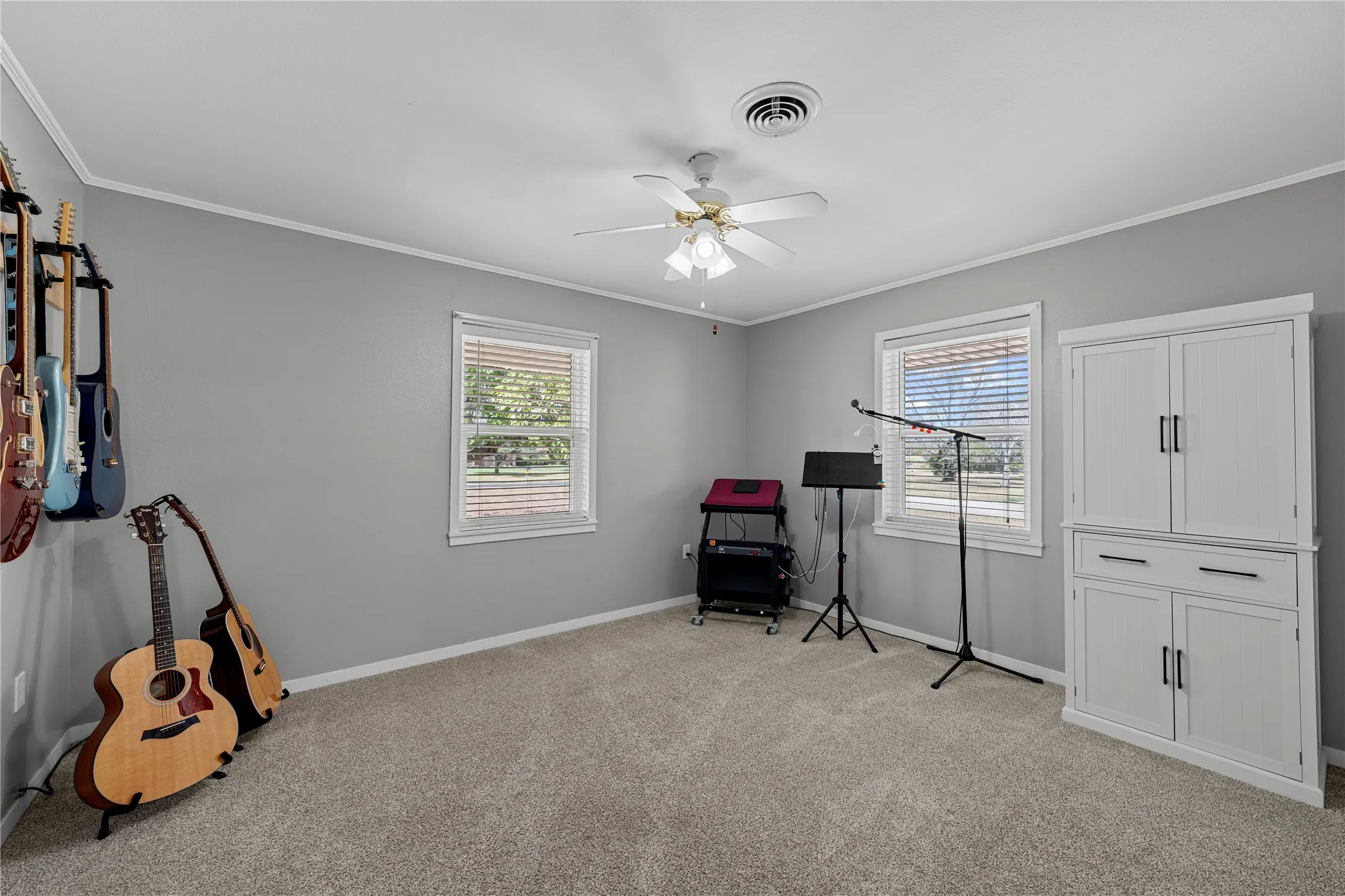 Gray painted walls, white crown molding, ceiling fan with light fixture, gray carpet flooring, and a built-in white cabinet with black hardware