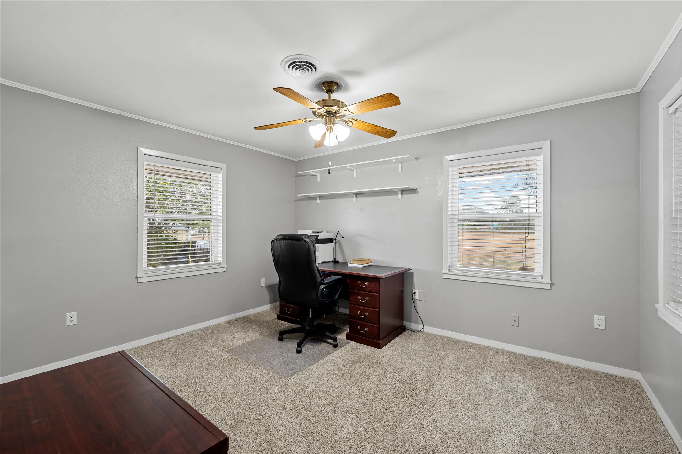 Recessed lighting fixture, ceiling fan, multiple windows with blinds, wall-mounted shelving, and carpet flooring