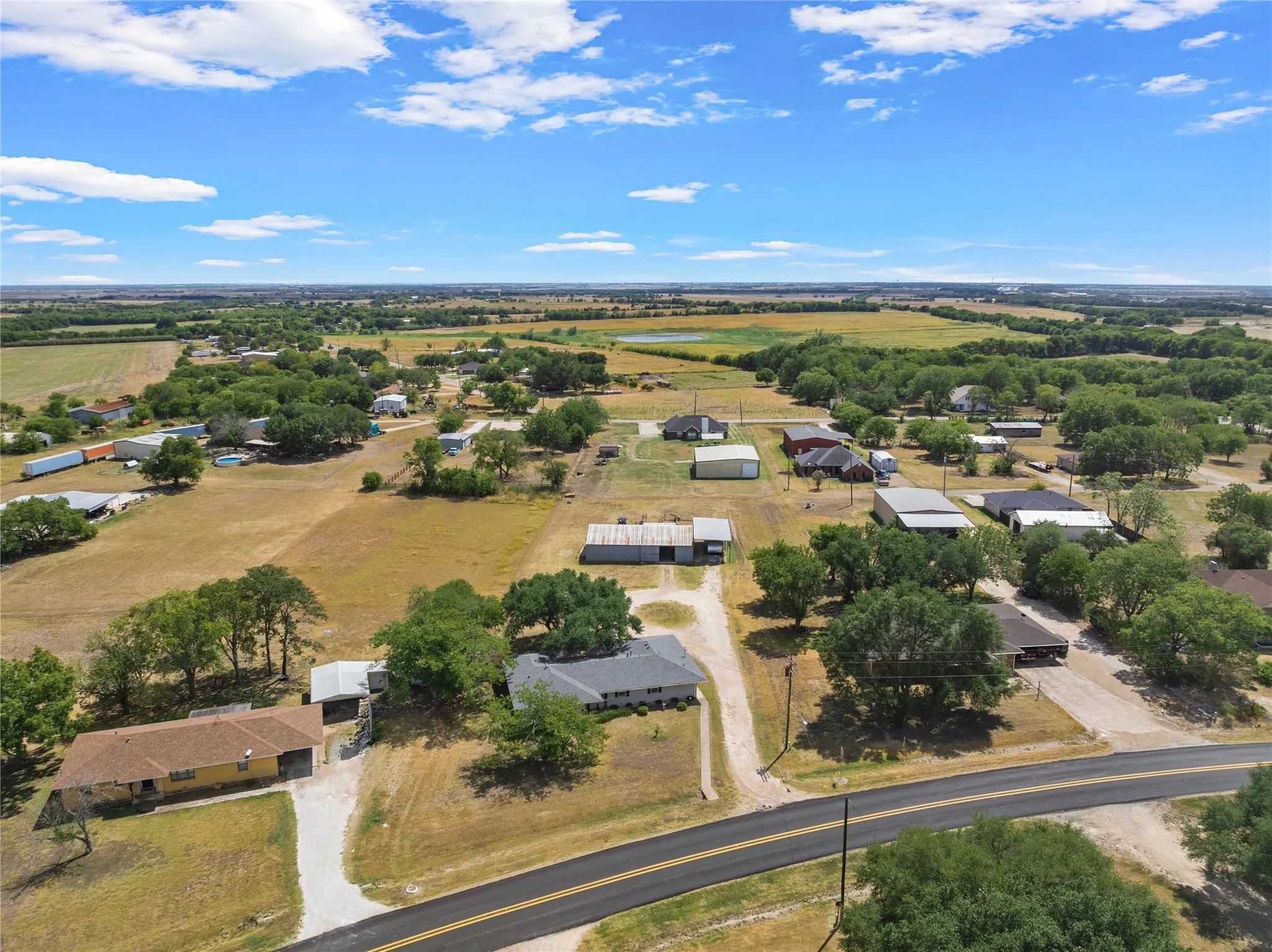 Expansive property featuring a paved road, scattered mature trees, and a distant field
