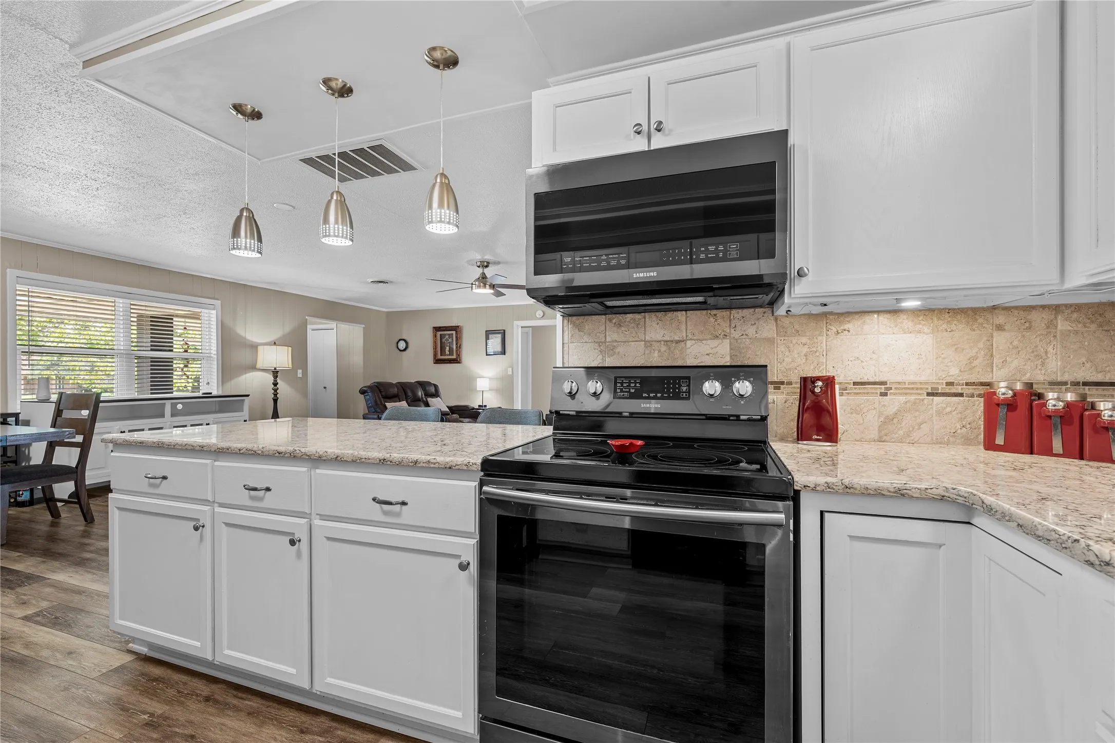 White cabinetry, granite countertops, and stainless steel appliances, complemented by a tiled backsplash and wood-finish flooring