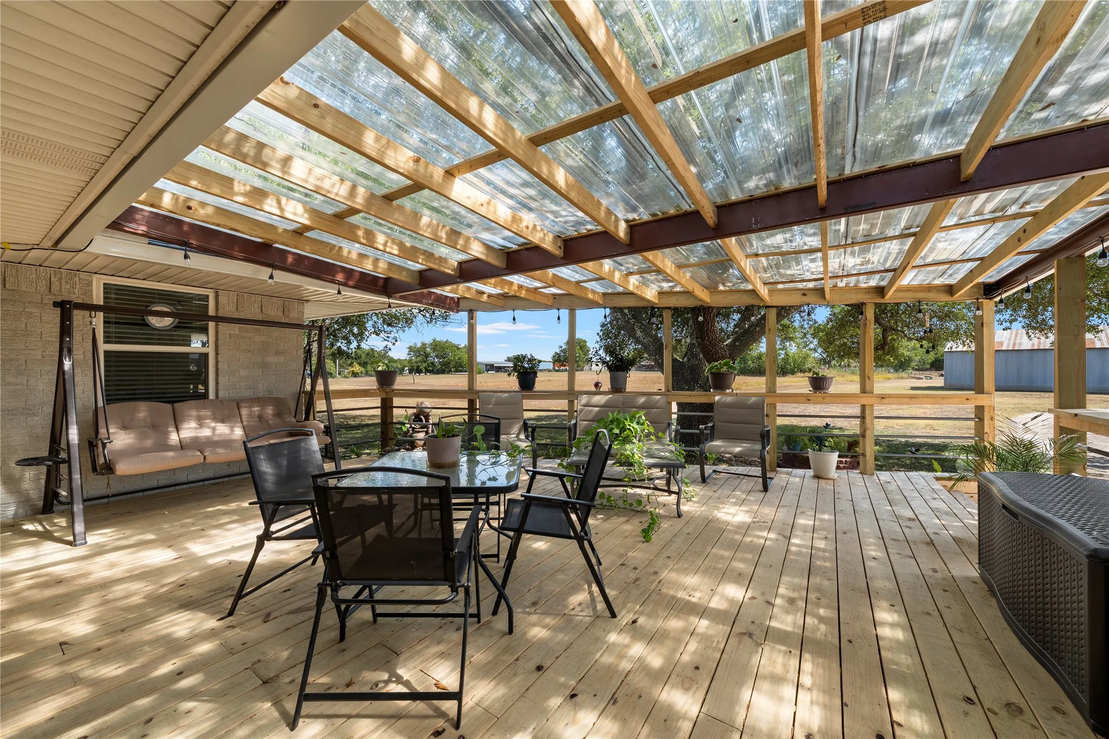 Expansive wood deck with a translucent corrugated roof and wood framing, featuring a built-in railing, and exterior wall with a window