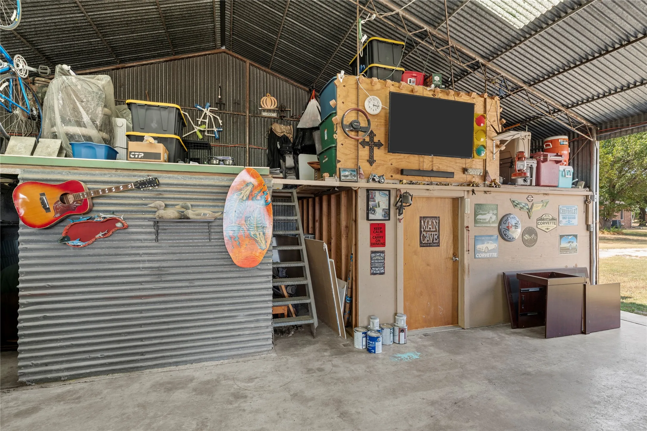 Corrugated metal walls and ceiling with an upper storage loft, a wood entry door, and concrete flooring