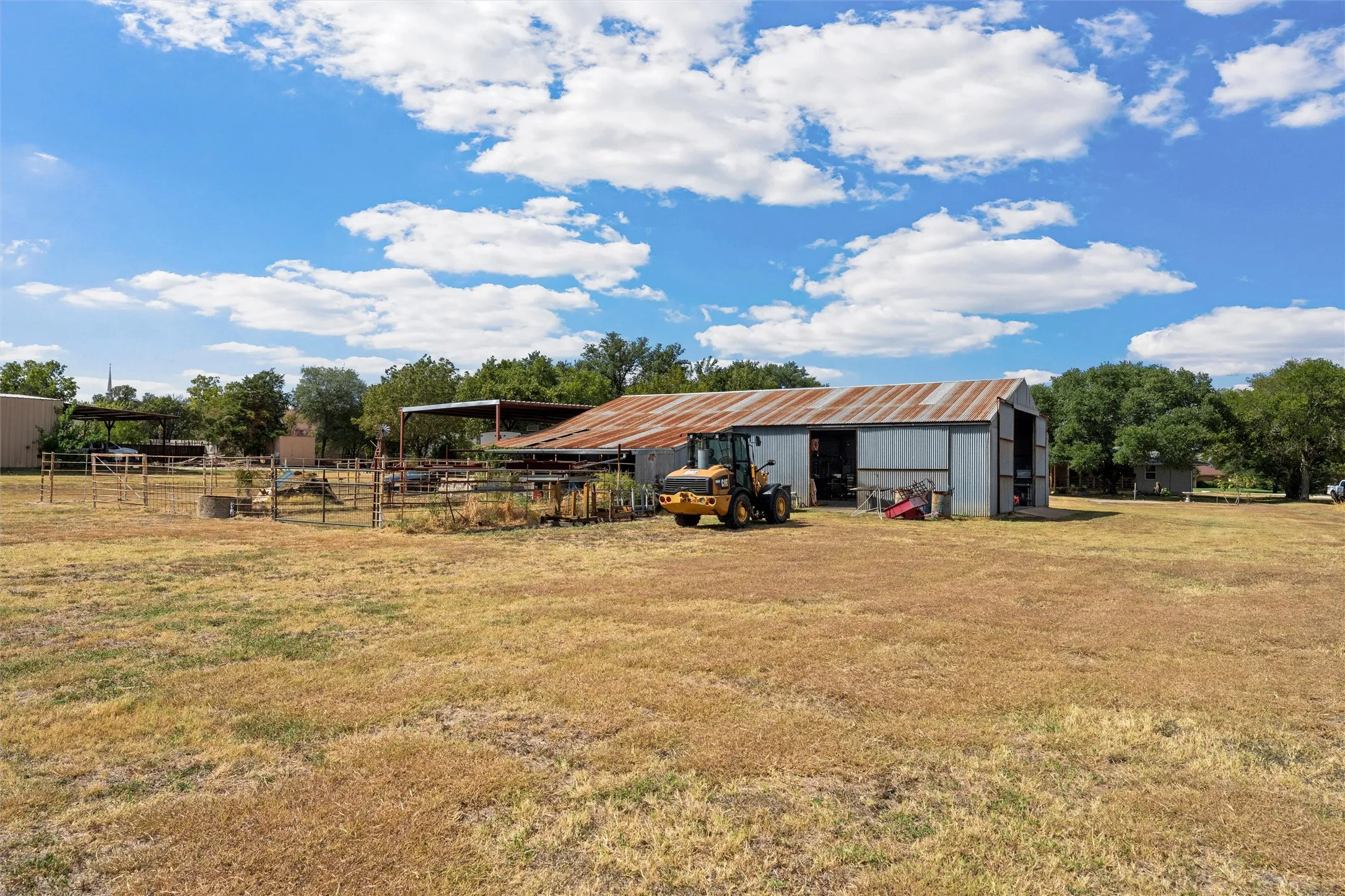 Expansive open field with outbuildings, fenced enclosures, and a large metal barn structure