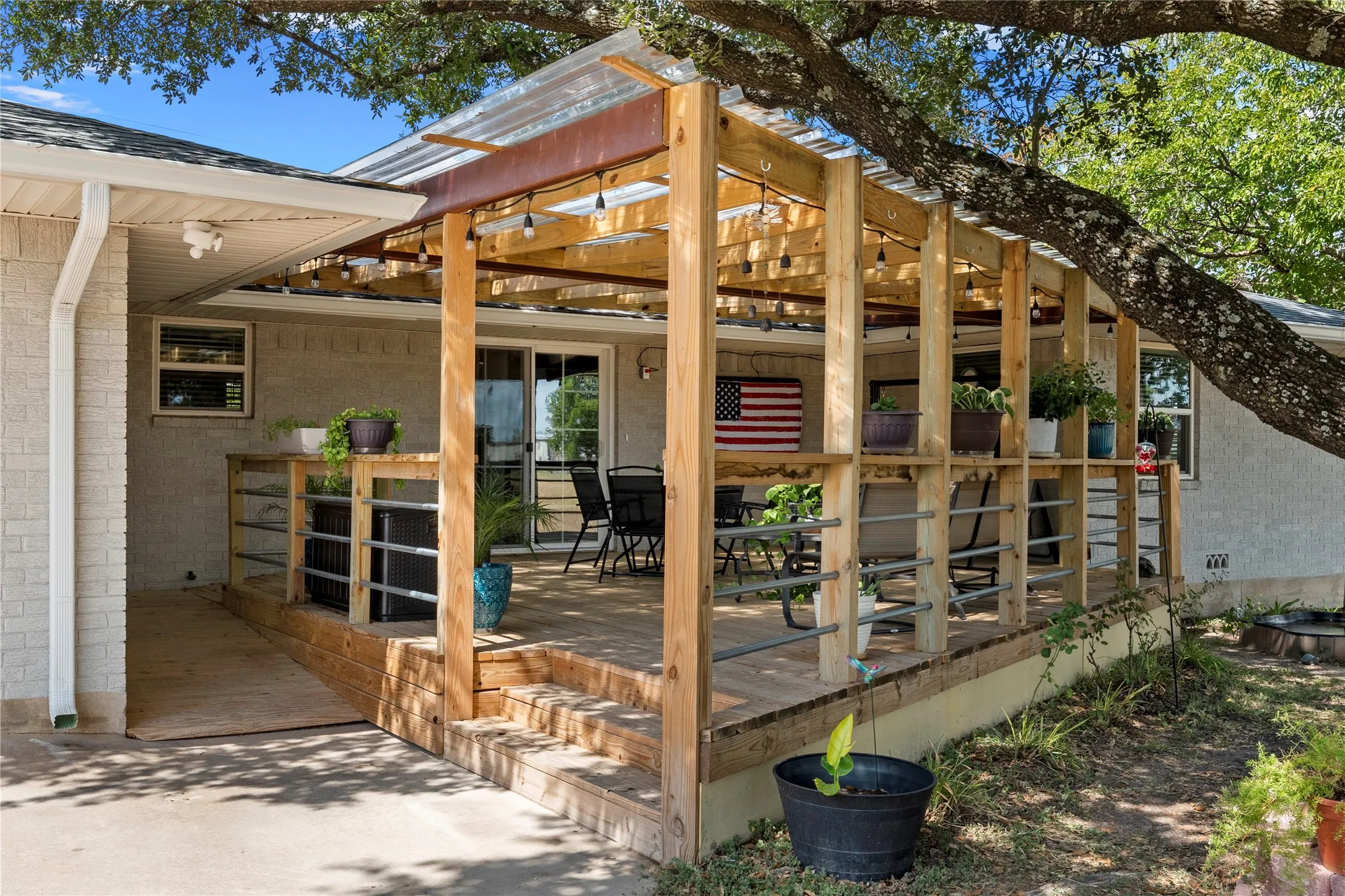 Expansive wood deck with a clear panel roof and string lighting, featuring a wood and metal railing