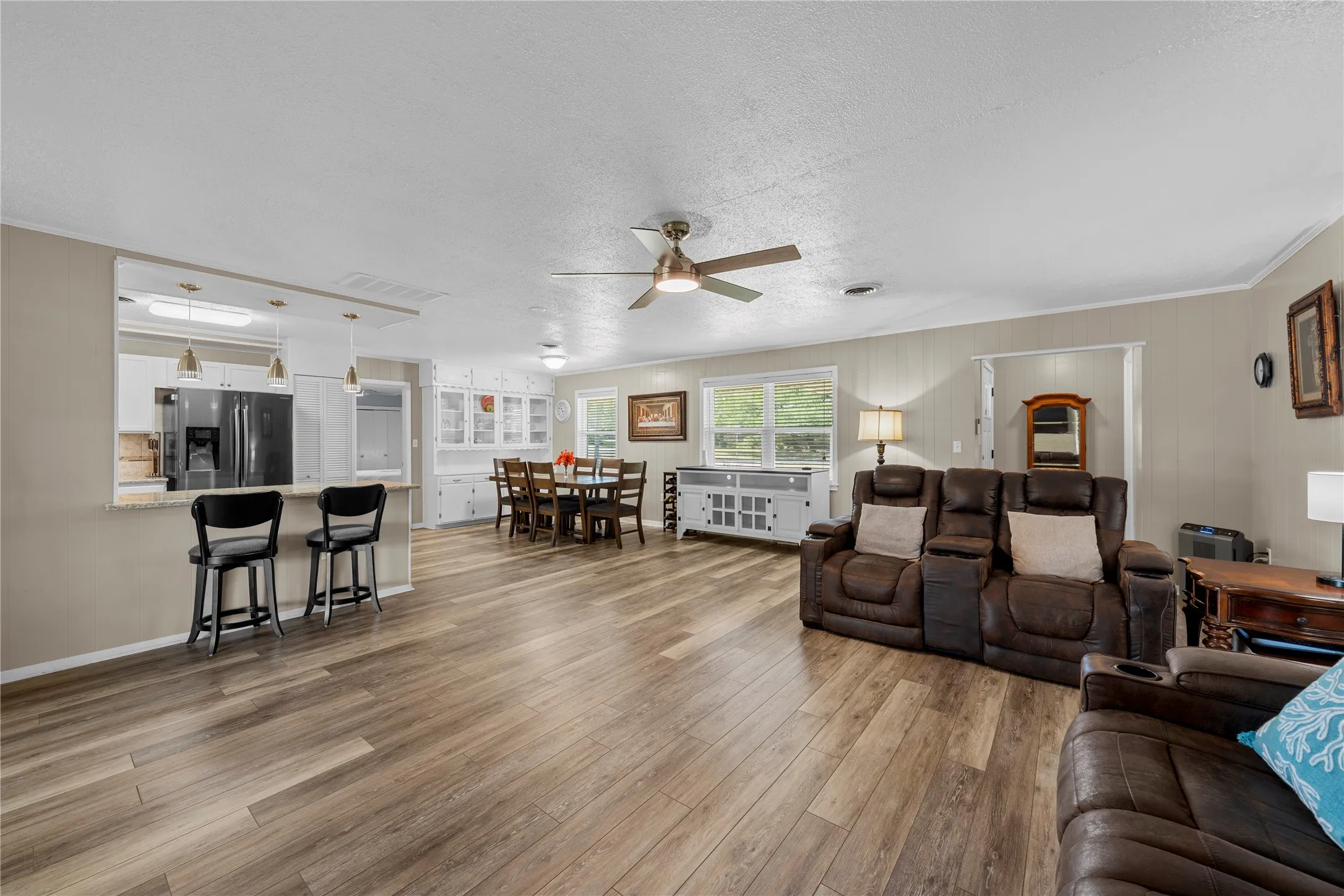 Wood-finish flooring throughout, ceiling fan with light fixture, breakfast bar with pendant lighting, white cabinetry, and multiple windows
