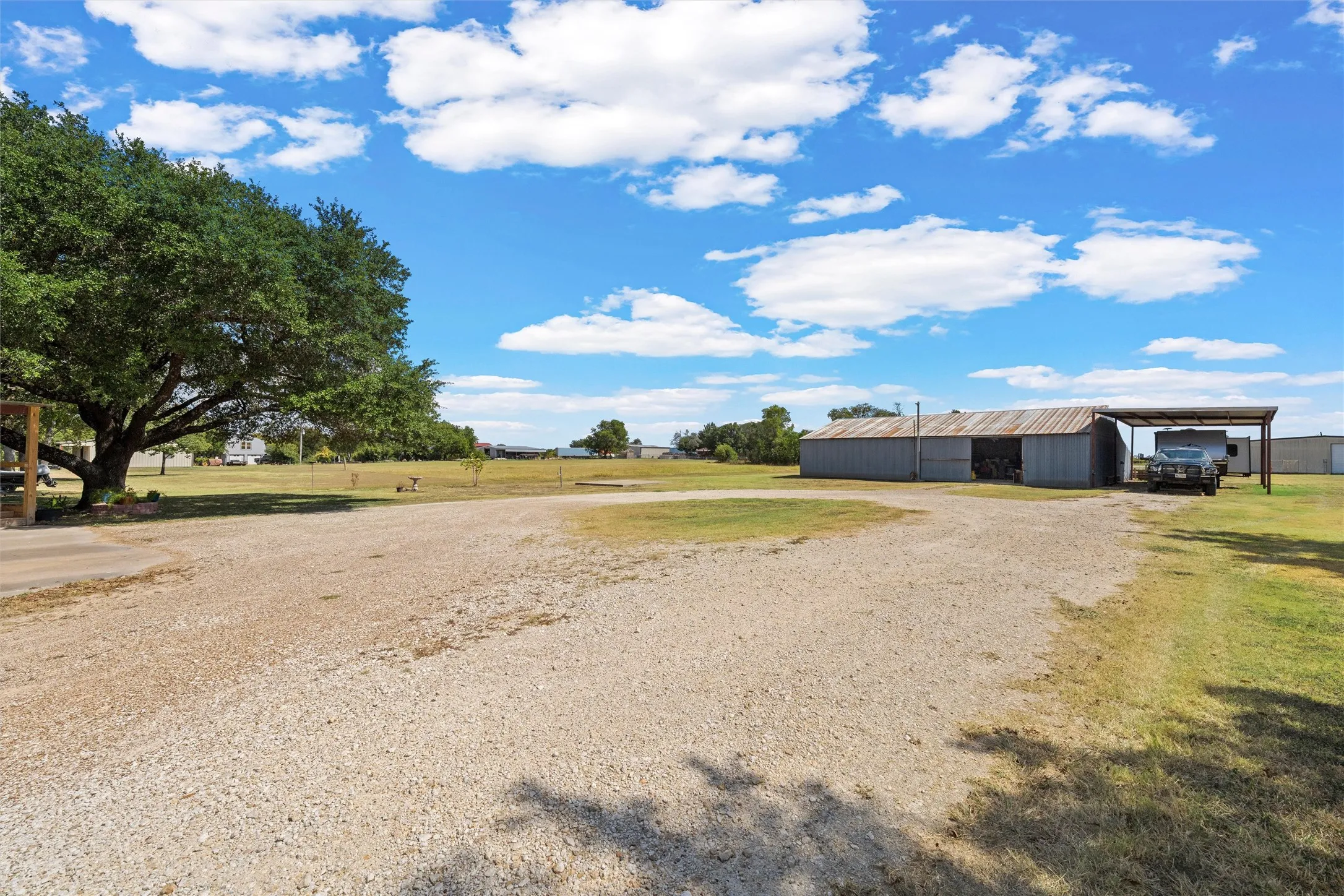 Expansive gravel driveway leading to a metal-sided outbuilding with an attached covered carport