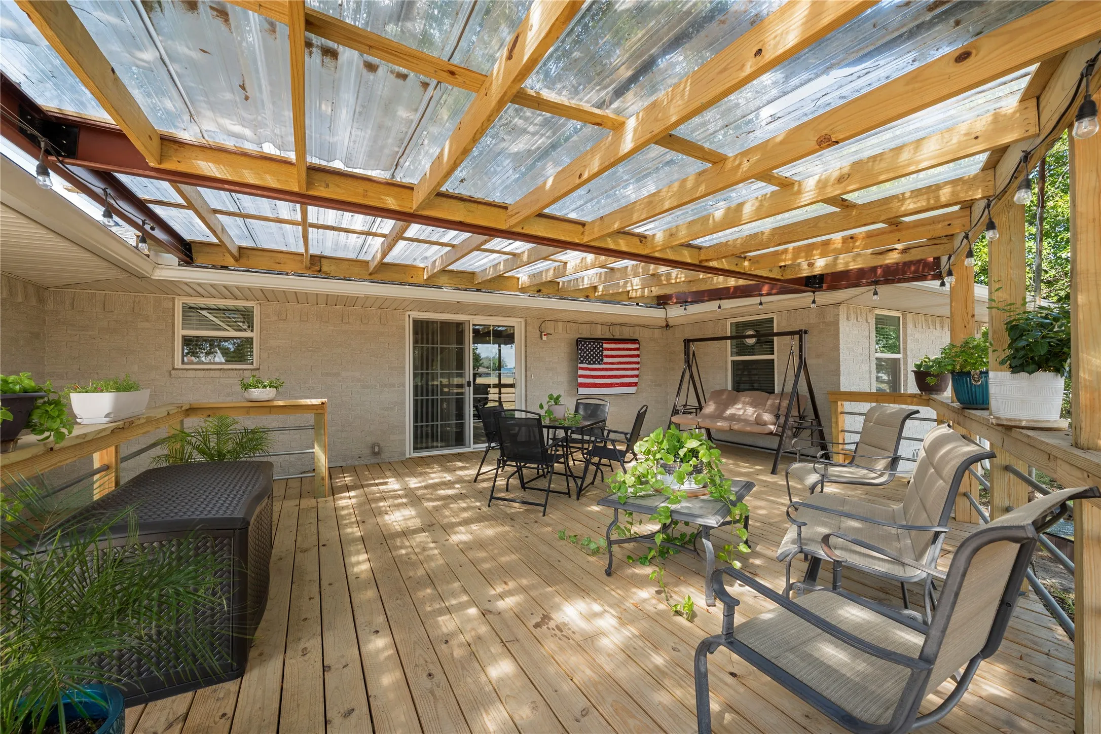 Expansive outdoor deck featuring wood flooring, a clear paneled overhead covering, and sliding glass doors