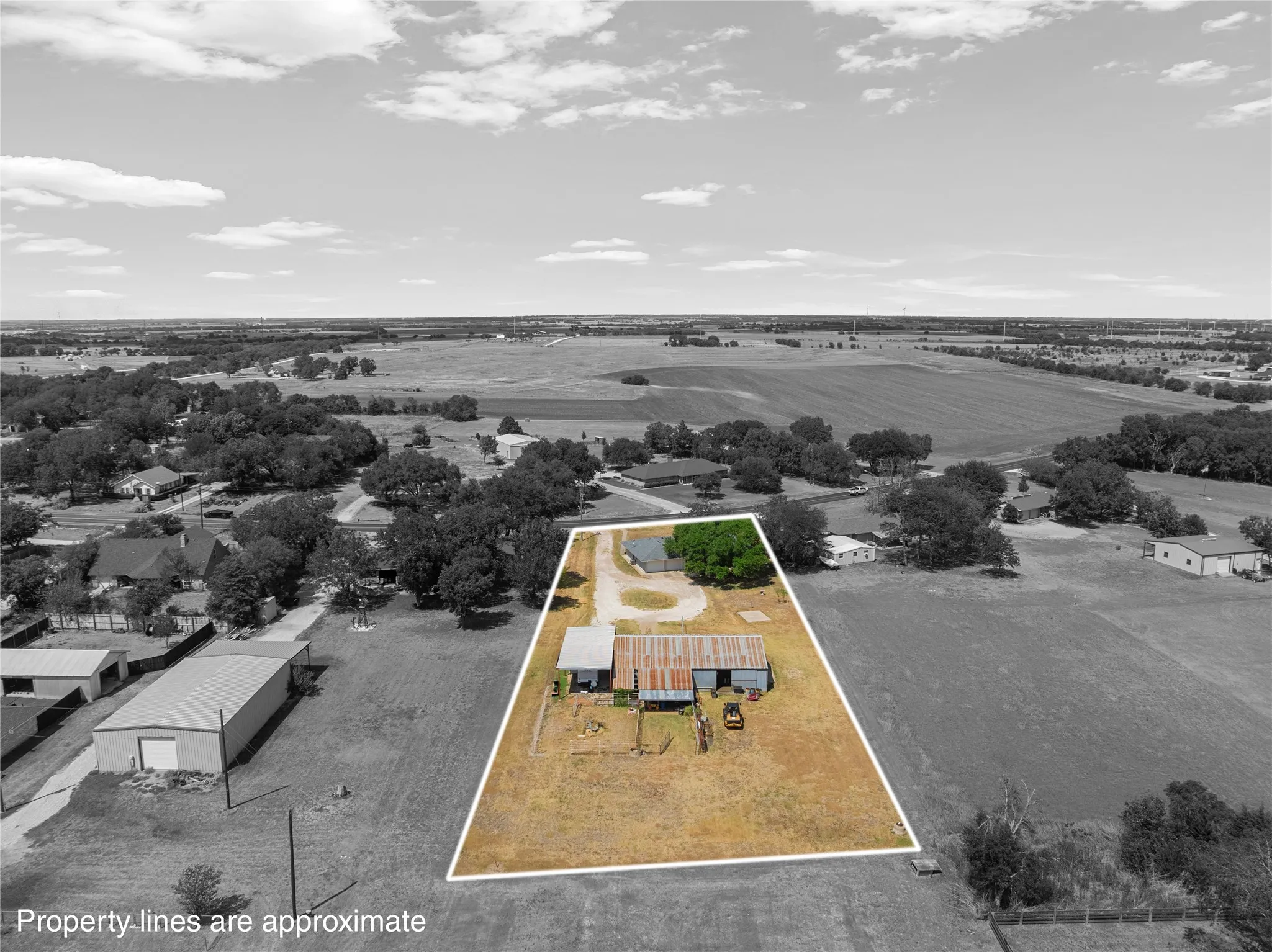 Aerial perspective of a property featuring a single-story residence, a large outbuilding with a metal roof, and an expansive dry grass area