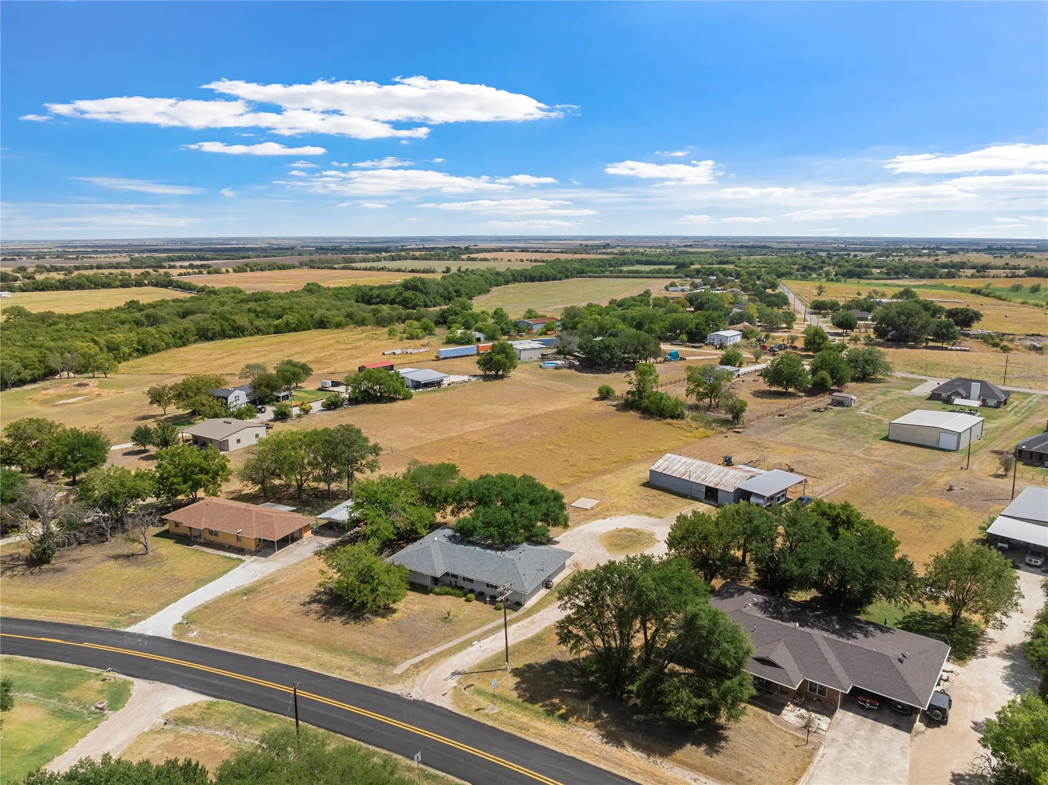 Aerial perspective showcasing expansive fields, dispersed residential structures, mature trees, and a paved road