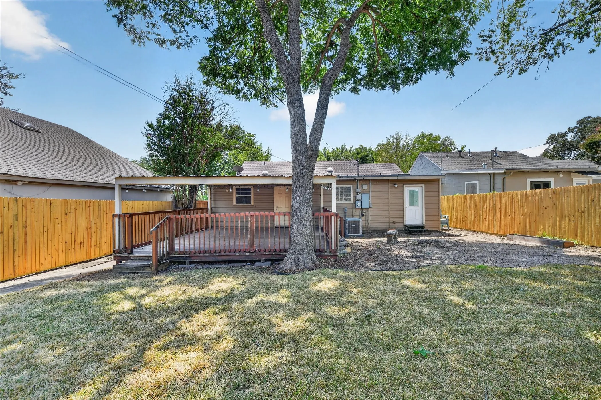 Expansive backyard featuring a large tree, wooden deck with railing, covered patio area, and new privacy fencing