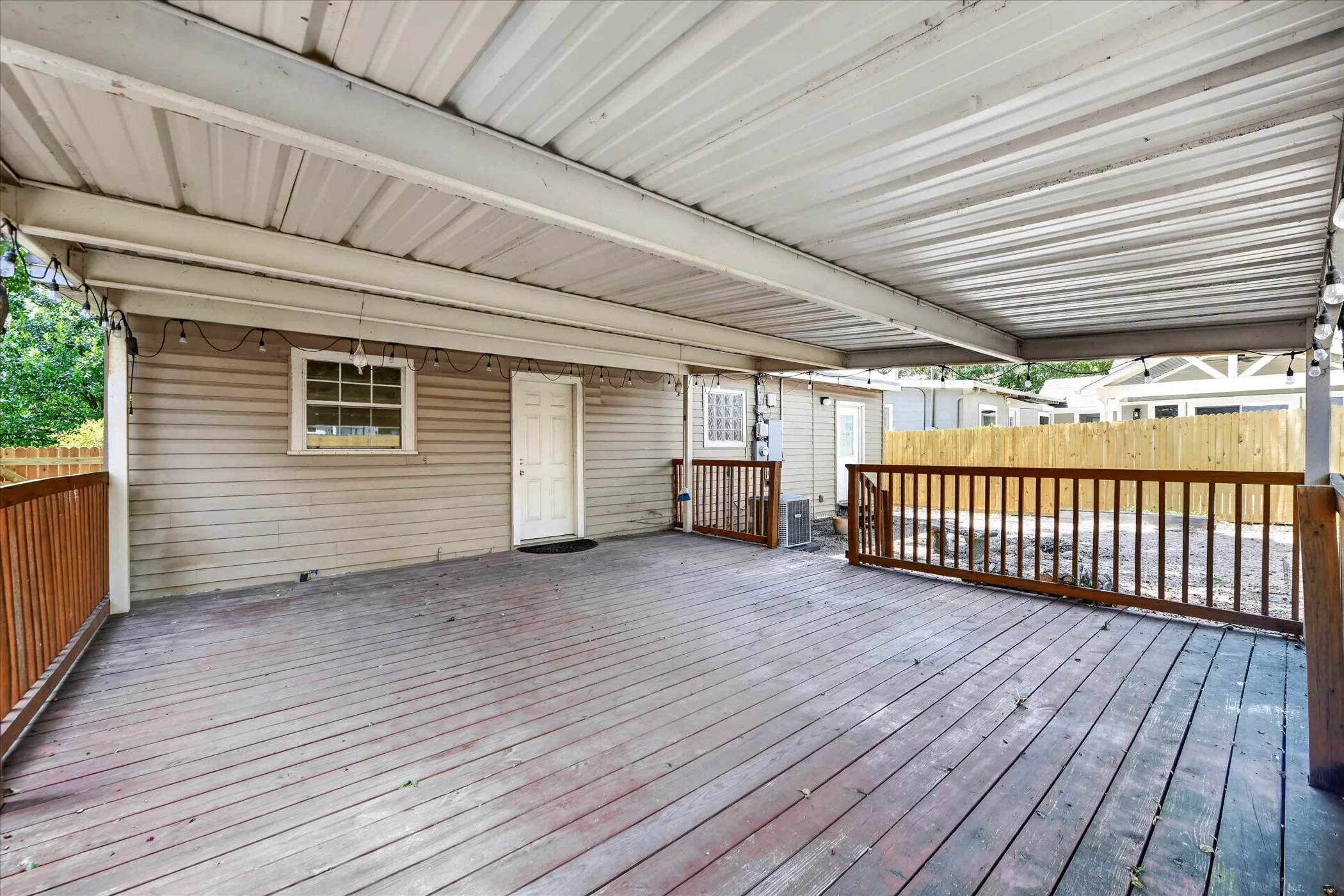 Expansive covered deck featuring wood decking, wood railings, and a corrugated metal​​‌​​​​‌​​‌‌​‌‌​​​‌‌​‌​‌​‌​​​‌​​ roof