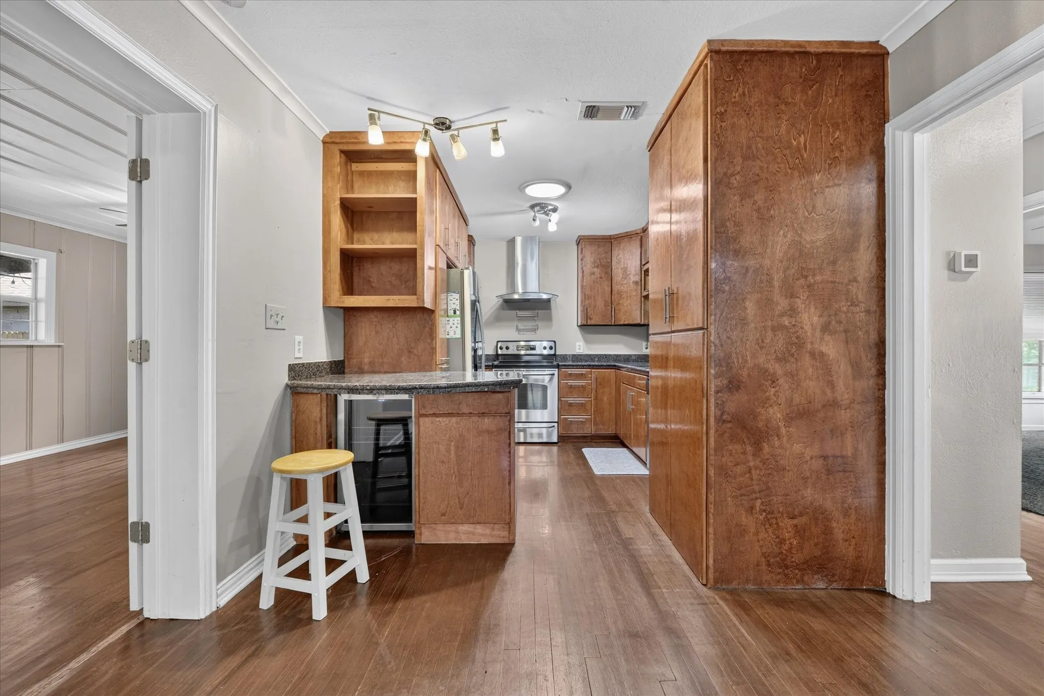Kitchen featuring wood-finish cabinetry, built-in shelving, stainless steel appliances, a counter-depth refrigerator, and wood-finish flooring