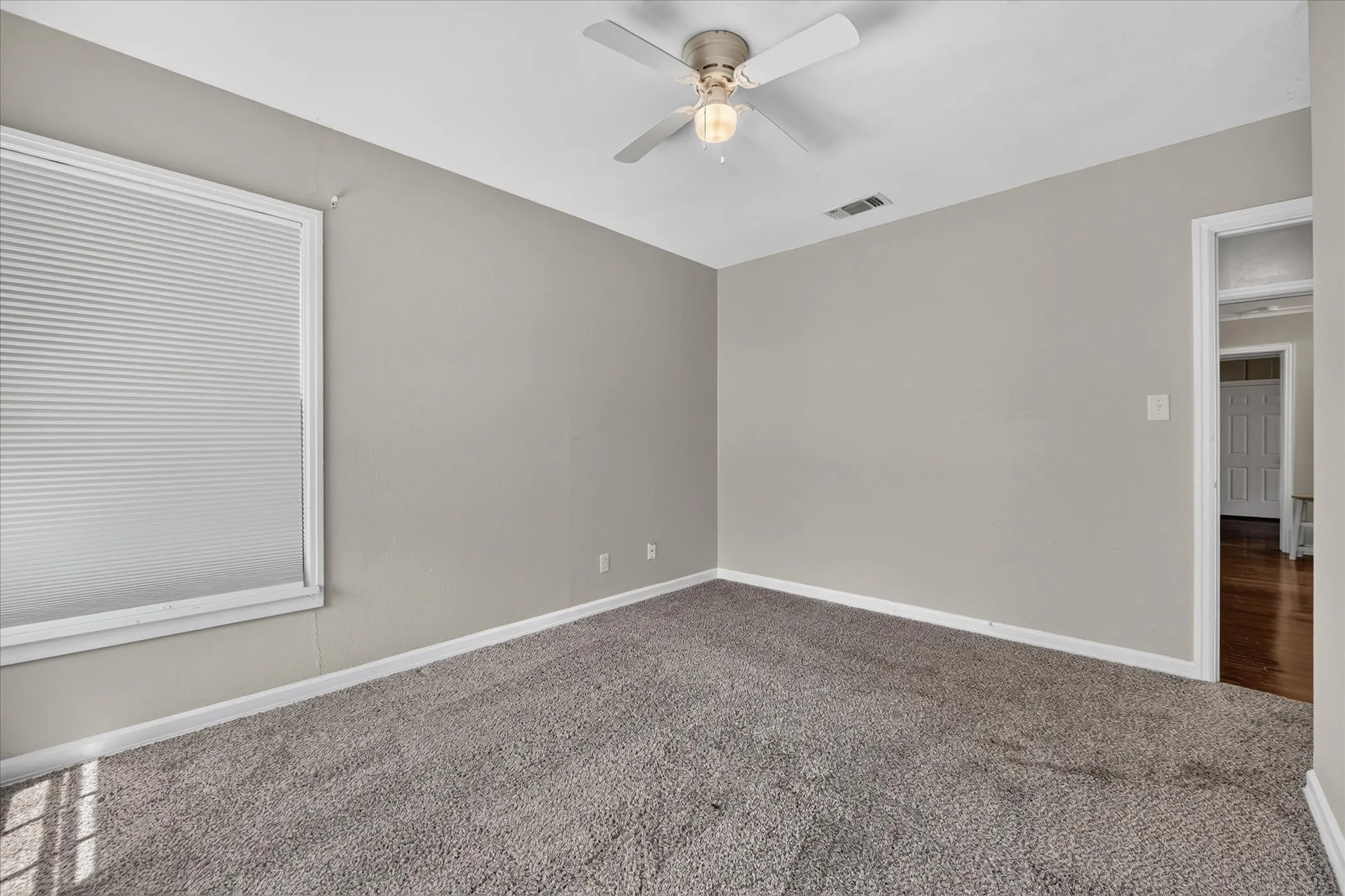 Neutral wall paint, ceiling fan with integrated lighting, window with horizontal blinds, and carpeted flooring