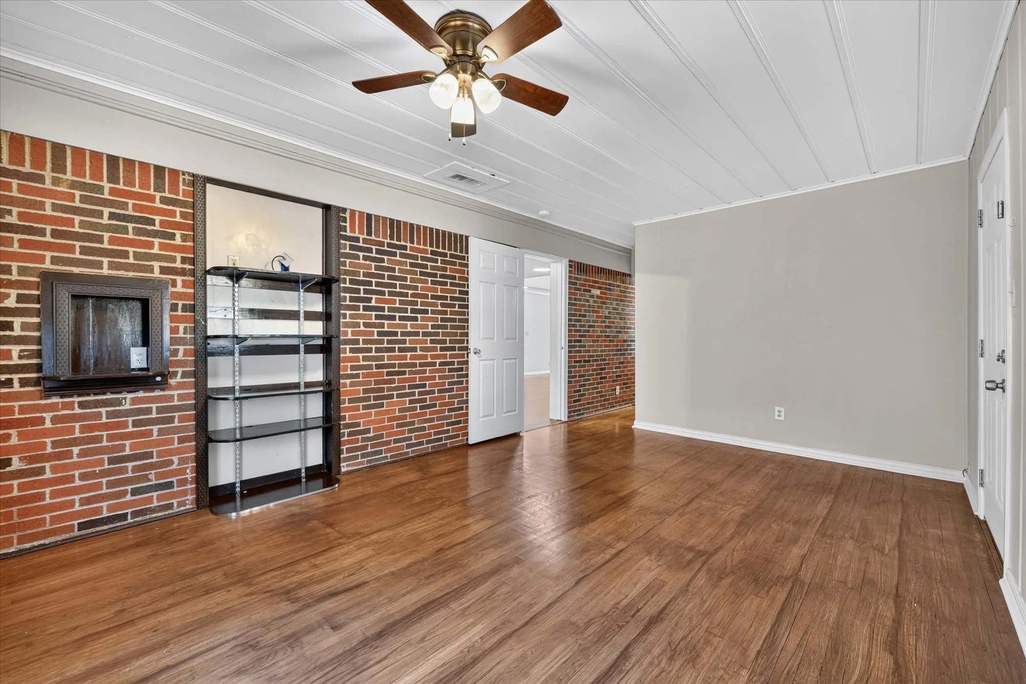 Wood-finish flooring, exposed brick accent wall, white beadboard ceiling, and a ceiling fan with light fixture