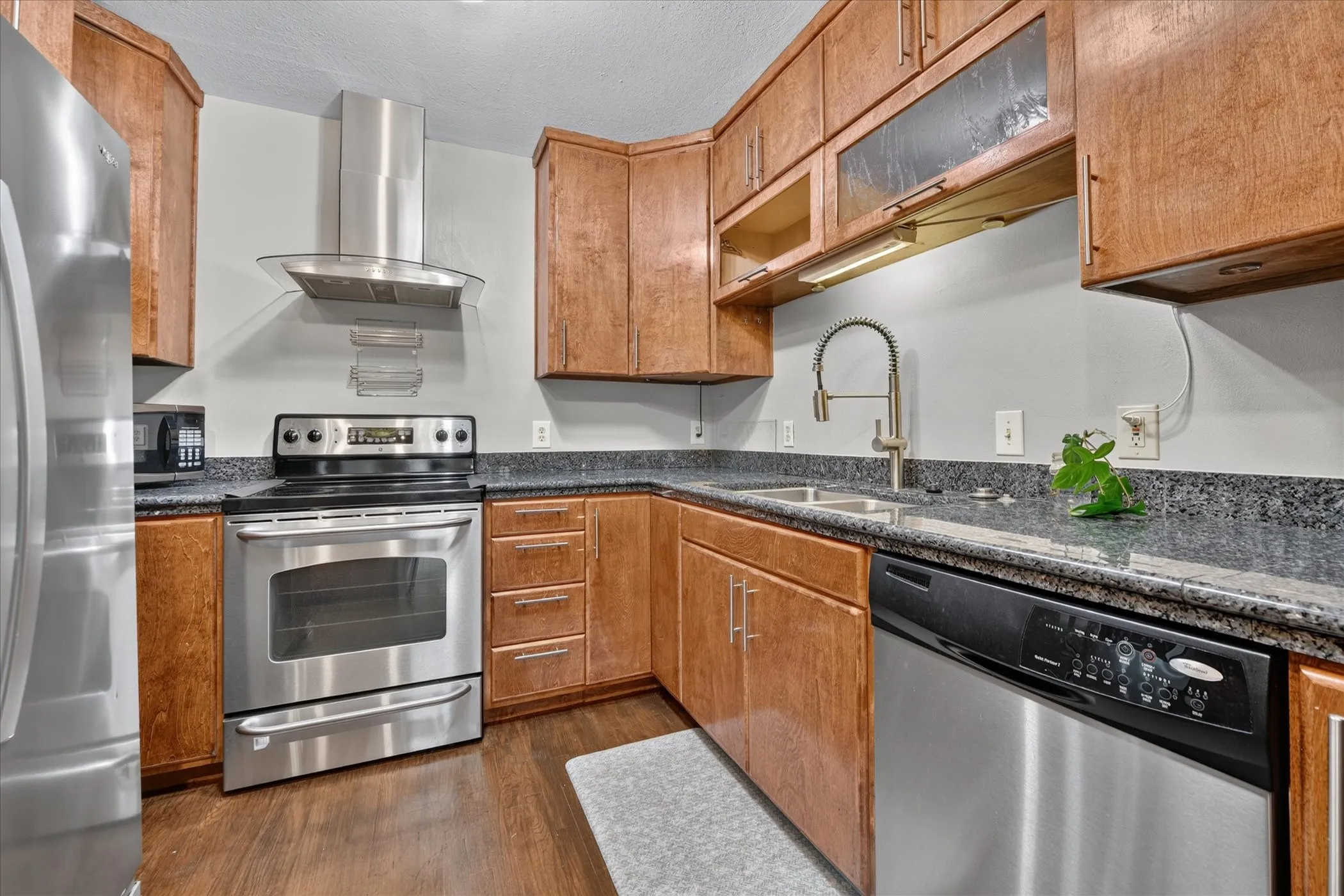 Kitchen featuring wood-finish cabinetry, stainless steel appliances, dark speckled countertops, and wood-finish flooring