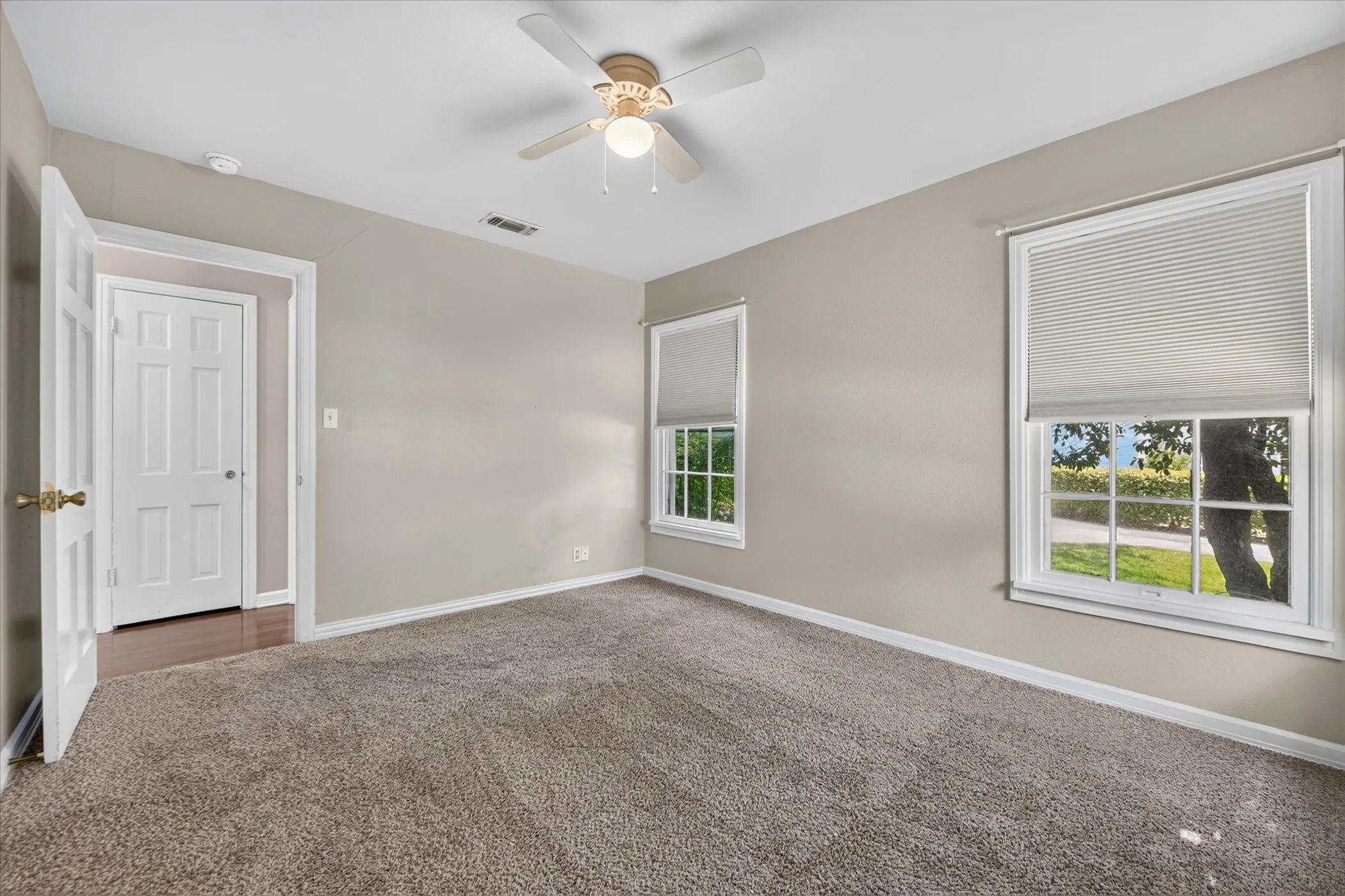Neutral wall color, light-toned carpeting, two windows with blinds, six-panel interior door, and a ceiling fan with integrated lighting
