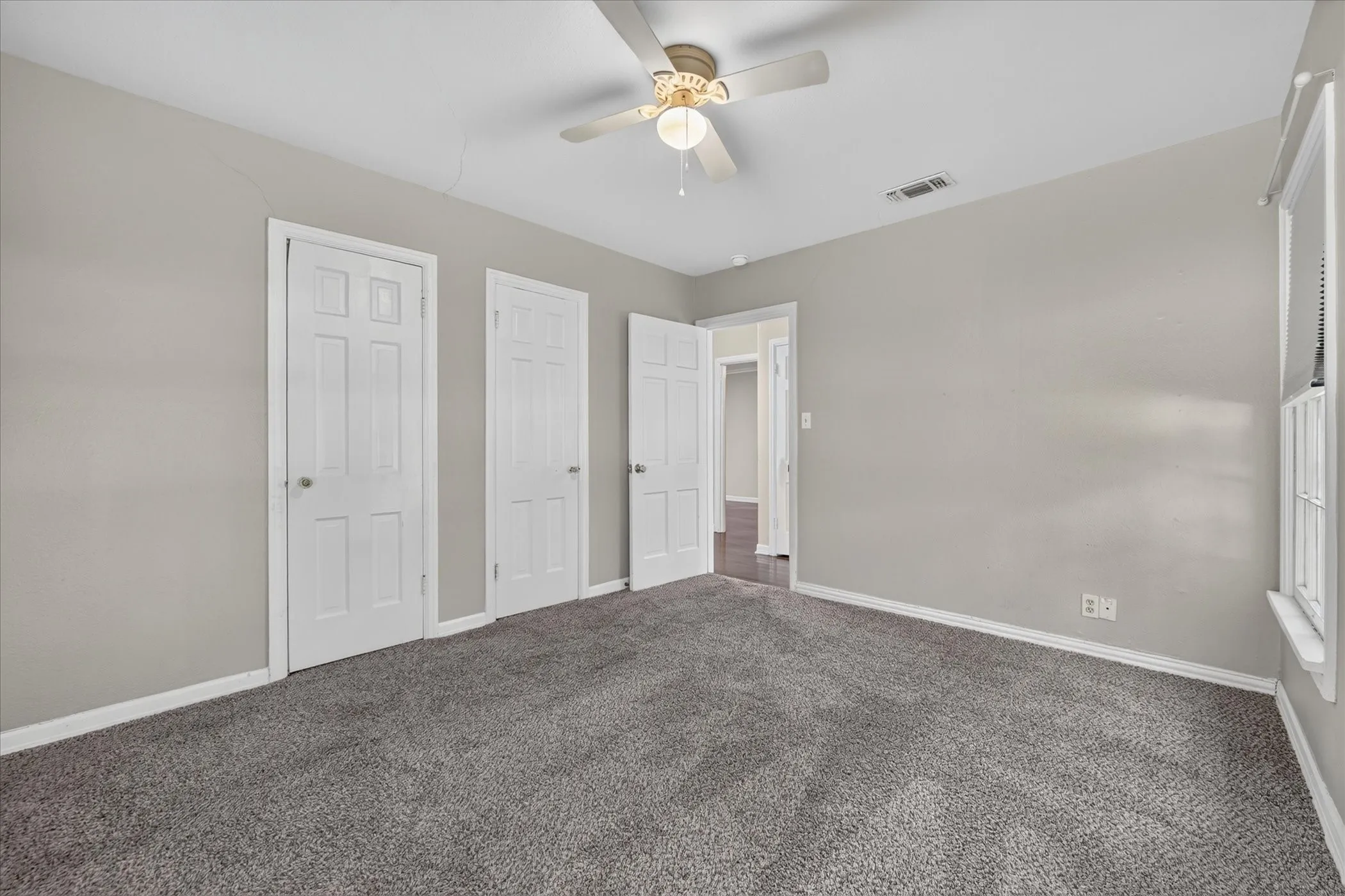 Neutral gray wall paint, gray carpet flooring, white trim, and a ceiling fan with integrated lighting